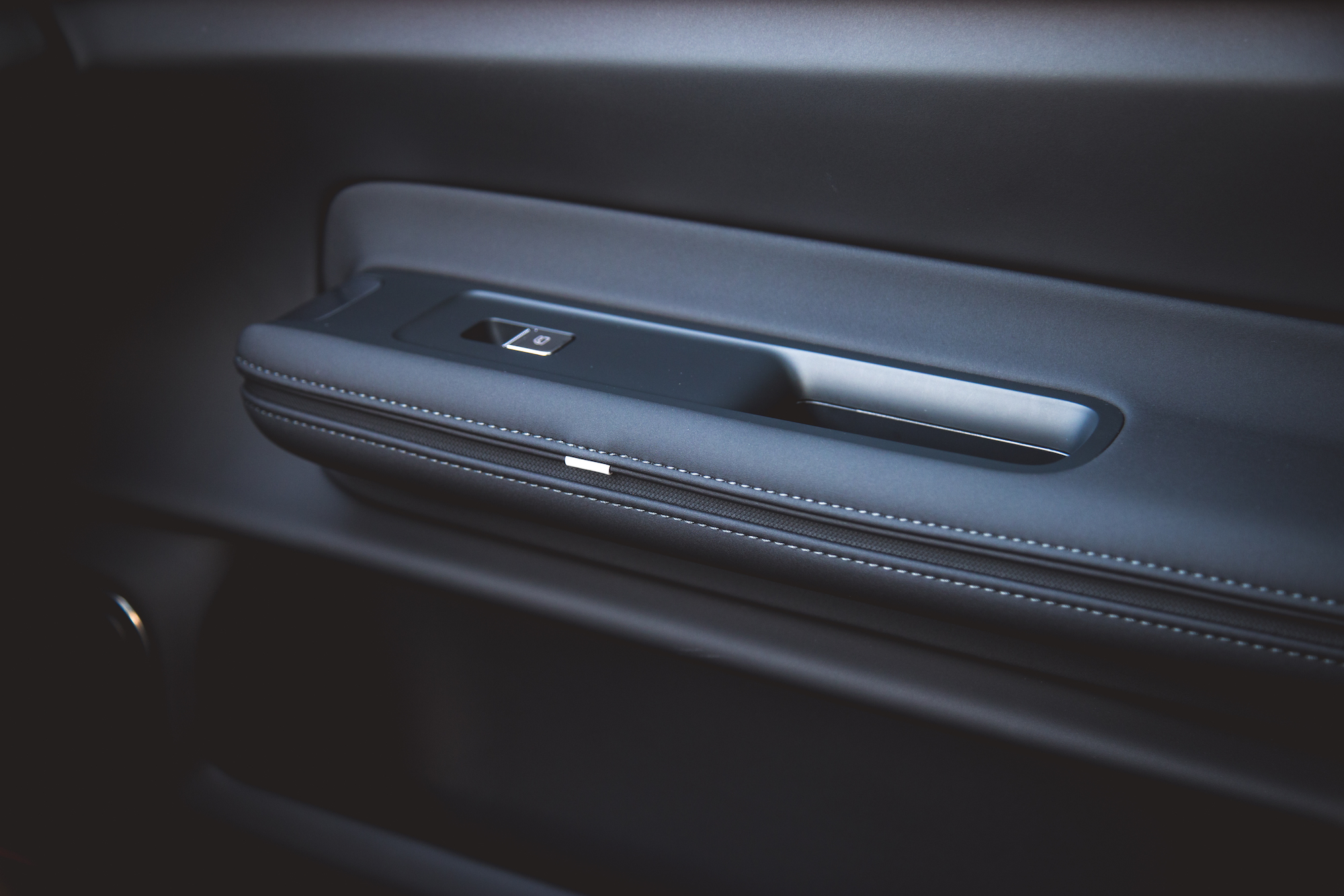 Primer plano del interior de la puerta de un automóvil con una elegante manija y apoyabrazos con detalles de costuras.