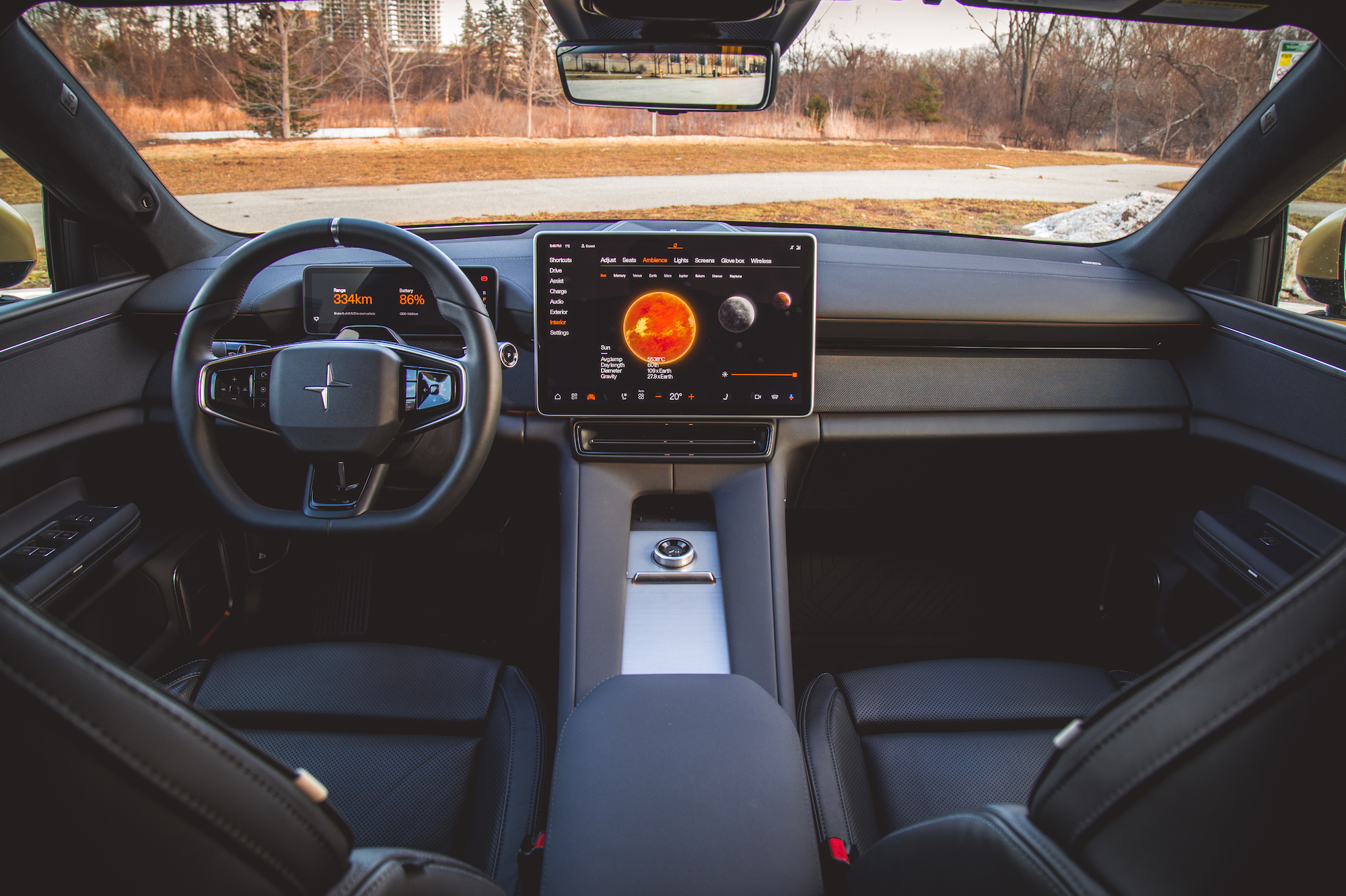 Vista interior de un automóvil moderno que muestra el volante, el tablero con una gran pantalla táctil y asientos de cuero negro. La pantalla muestra información de navegación y un gráfico planetario.