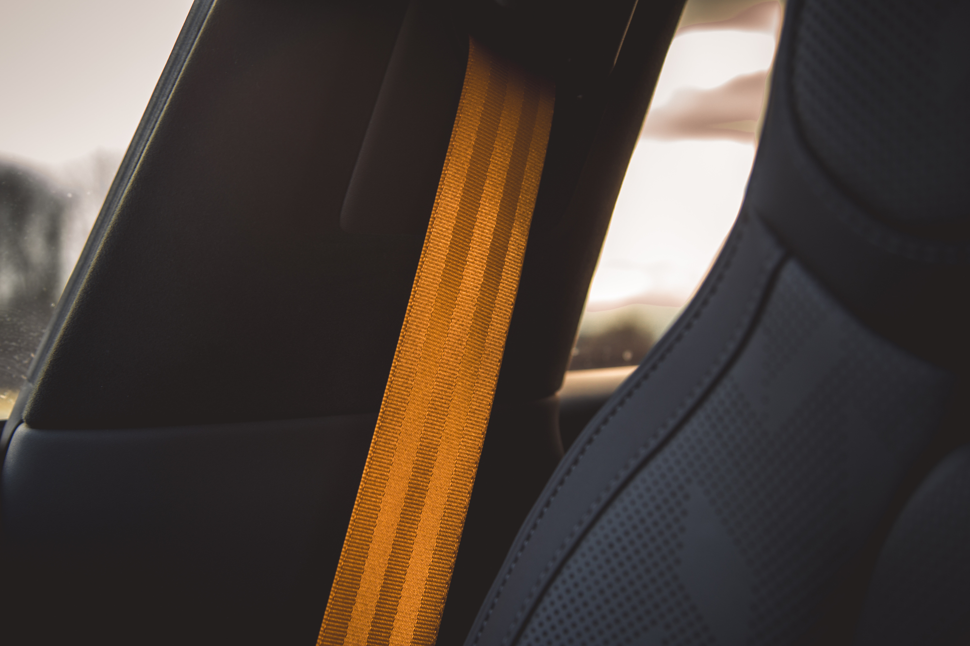 Primer plano del cinturón de seguridad de un coche en color naranja, colocado junto al asiento y al diseño interior del vehículo.