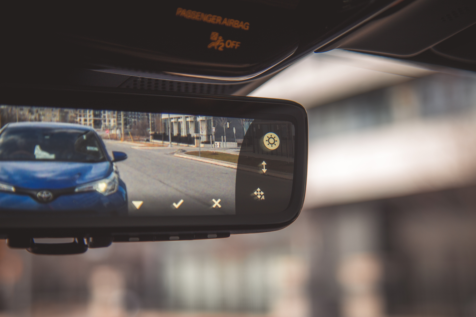 Vista de la pantalla de la cámara retrovisora ​​de un automóvil, que muestra un automóvil azul en una carretera con íconos de control visibles en la pantalla.
