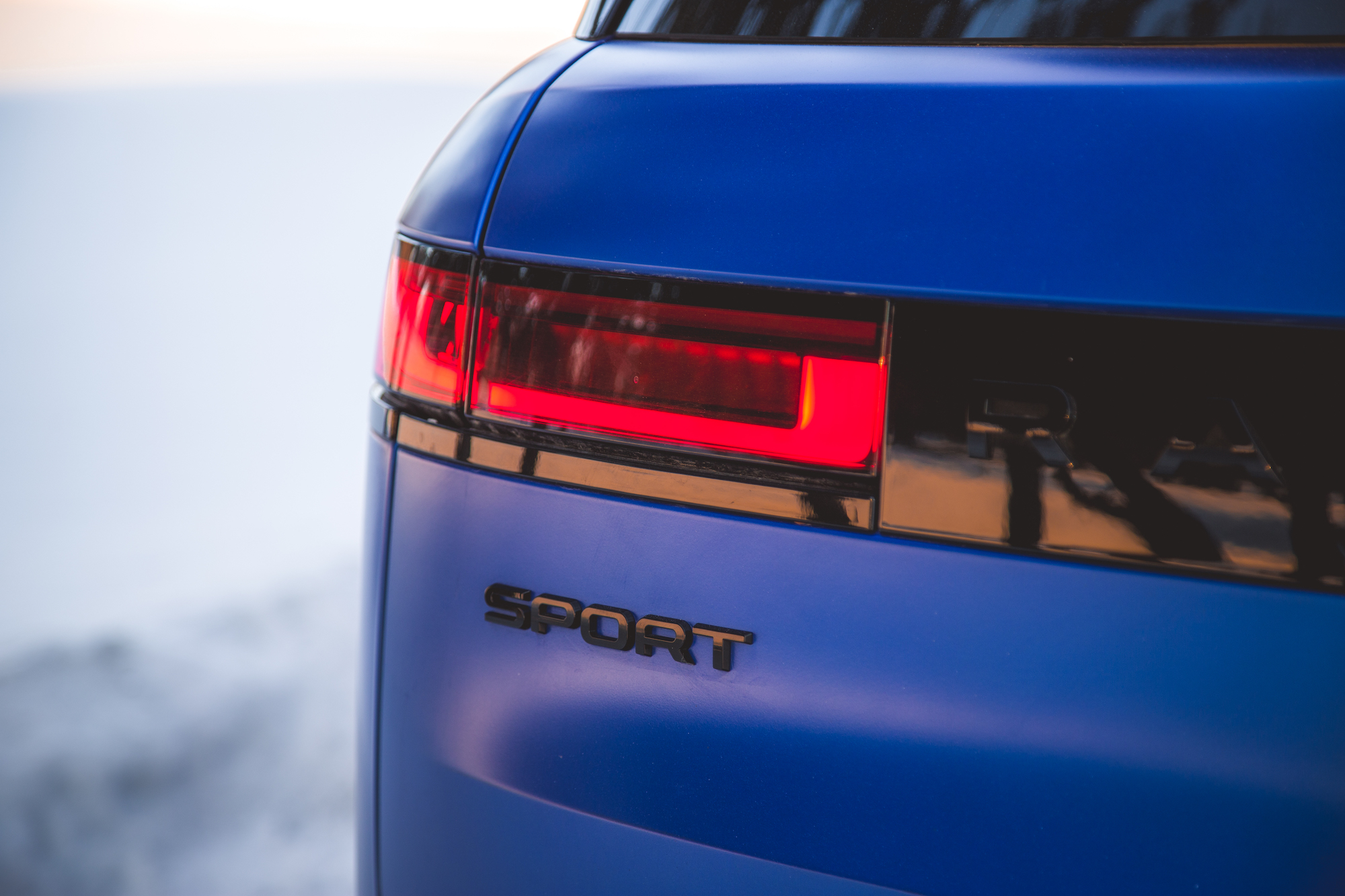Close-up of the rear of a blue sports car showcasing the taillight and the 'SPORT' emblem on the back.