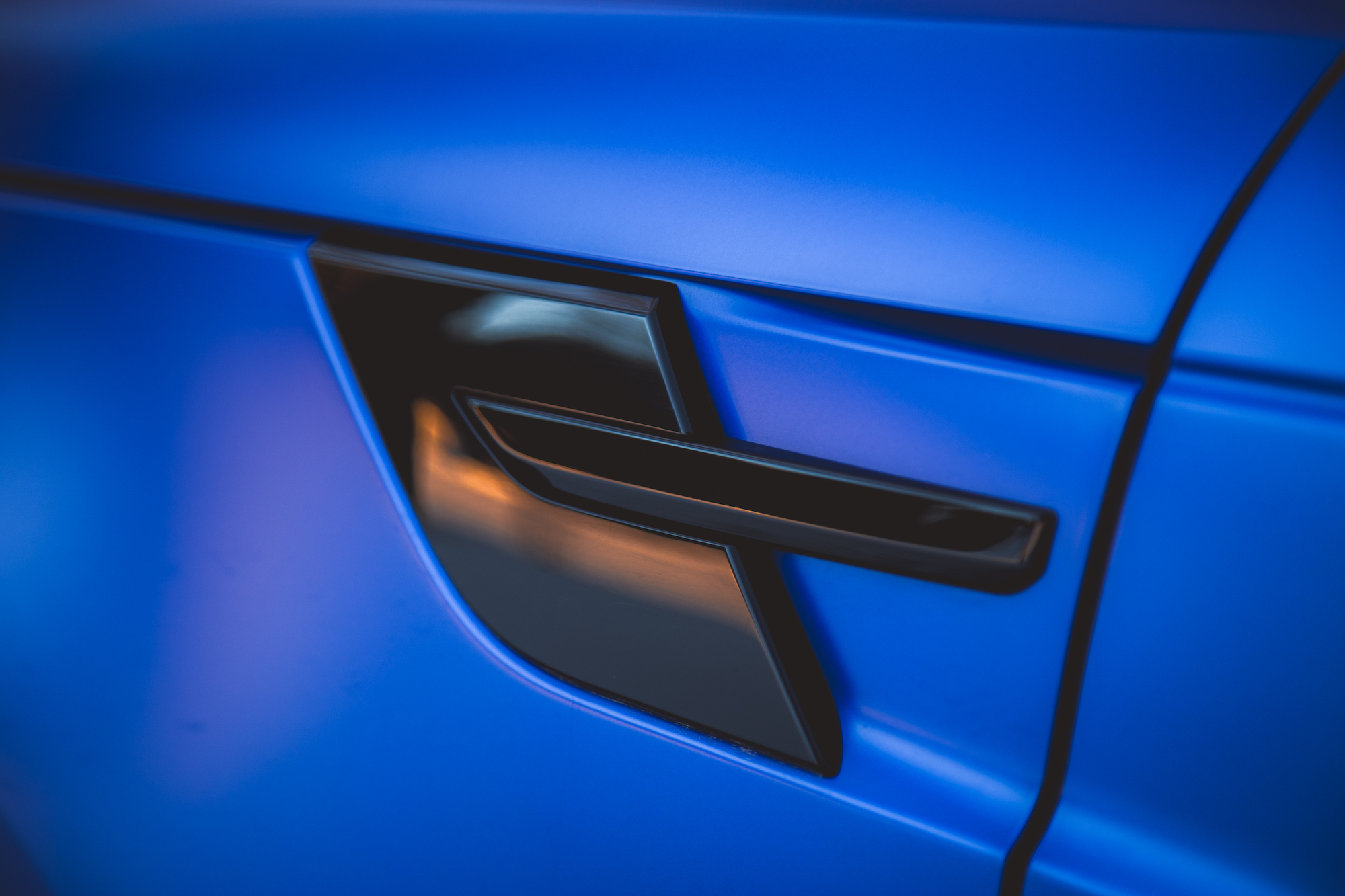 Close-up of a blue car door handle with a black accent panel.