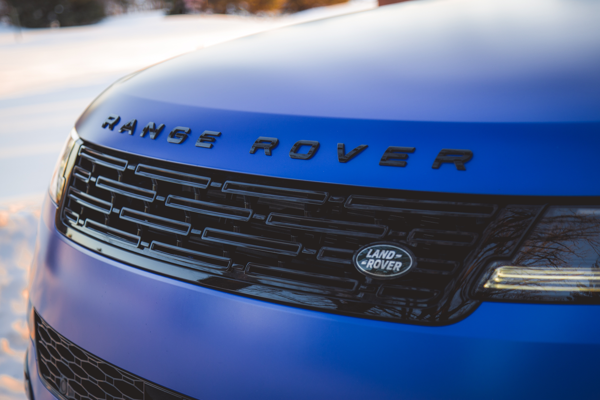 Close-up of a Range Rover front grille with the logo and dark accents on a snowy background.