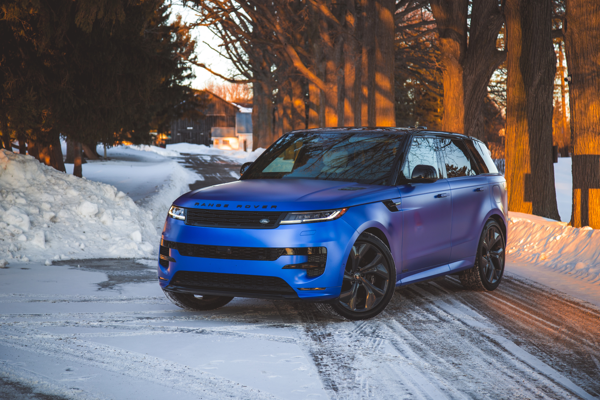 A blue matte-finished Range Rover parked on a snowy road, surrounded by trees and a sunset glow.