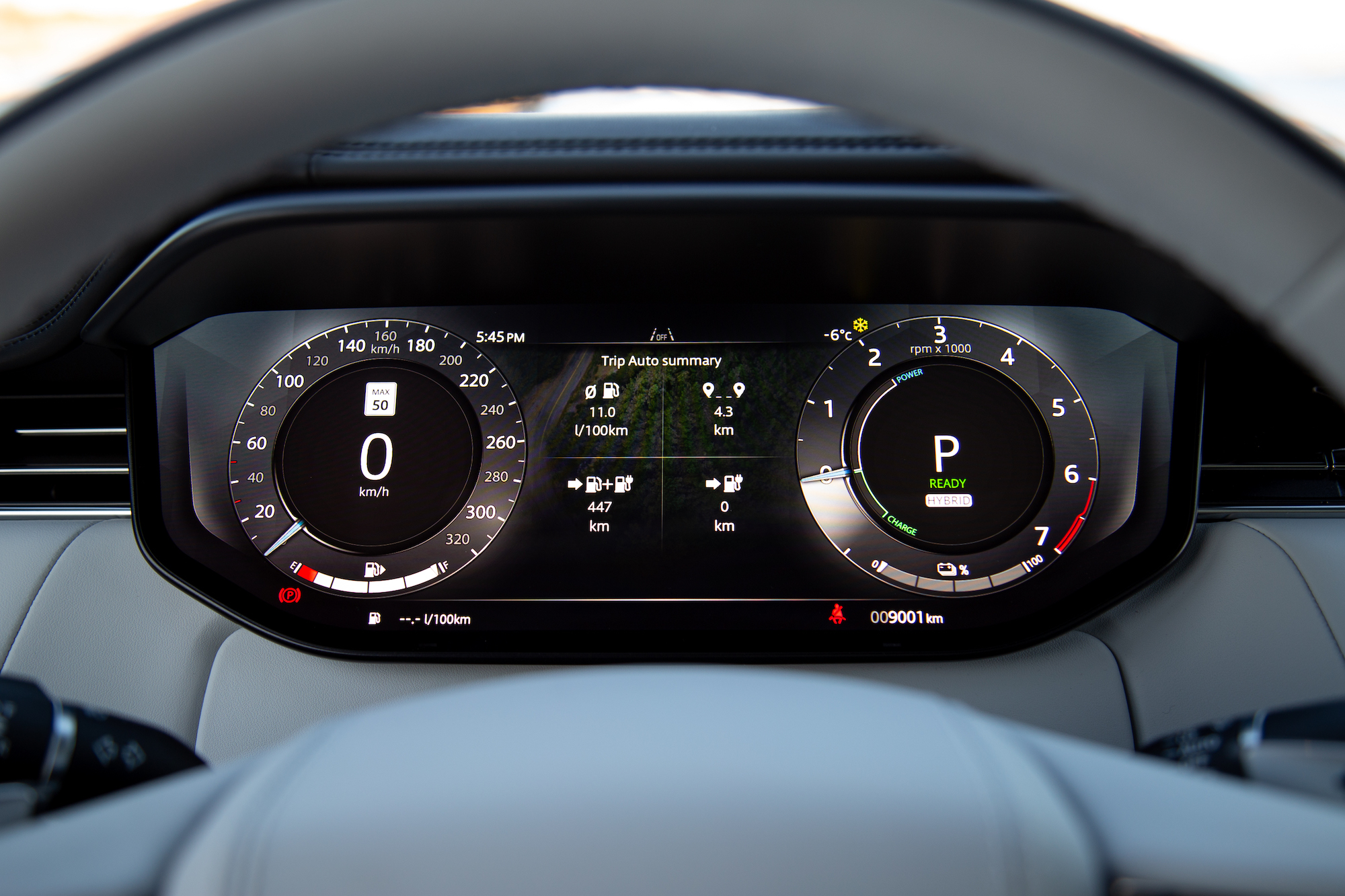 Dashboard display of a modern hybrid vehicle showing speedometer at 0 km/h, trip summary, fuel consumption, and gear indicator.