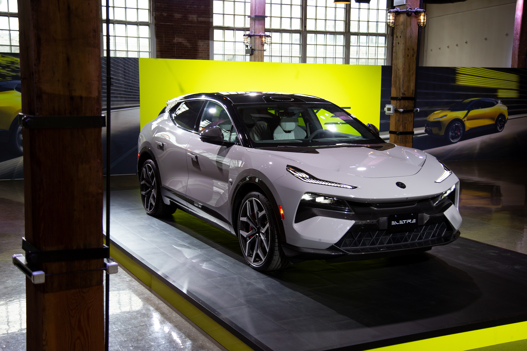 Un automóvil eléctrico elegante y moderno exhibido en un escenario con una iluminación de fondo de color amarillo brillante y una decoración de estilo industrial, que muestra su diseño y características.