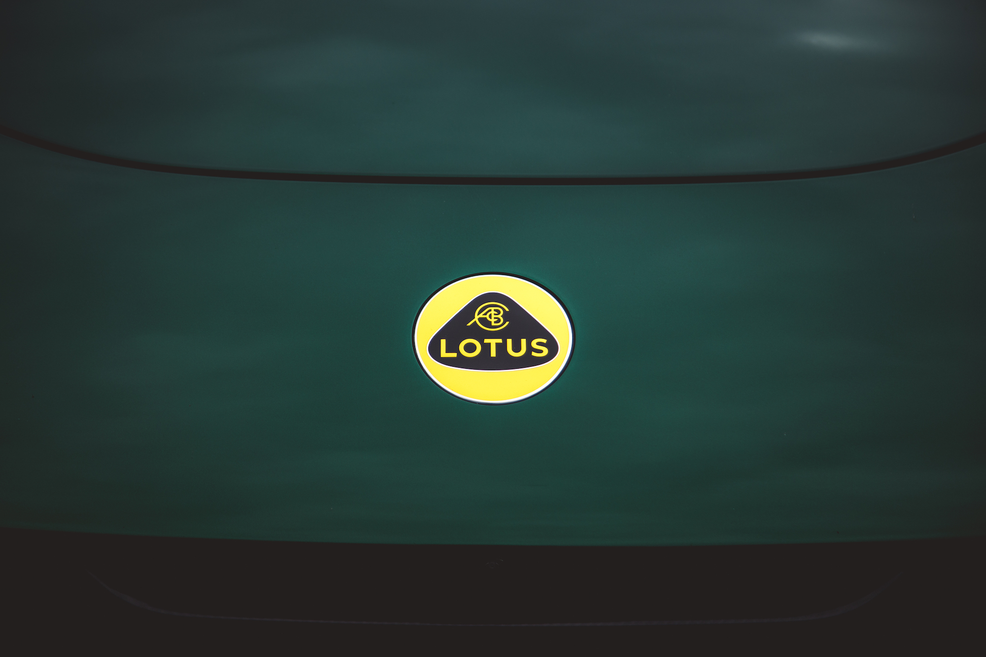 Primer plano de la insignia de un automóvil Lotus sobre el capó de un automóvil de color verde oscuro.
