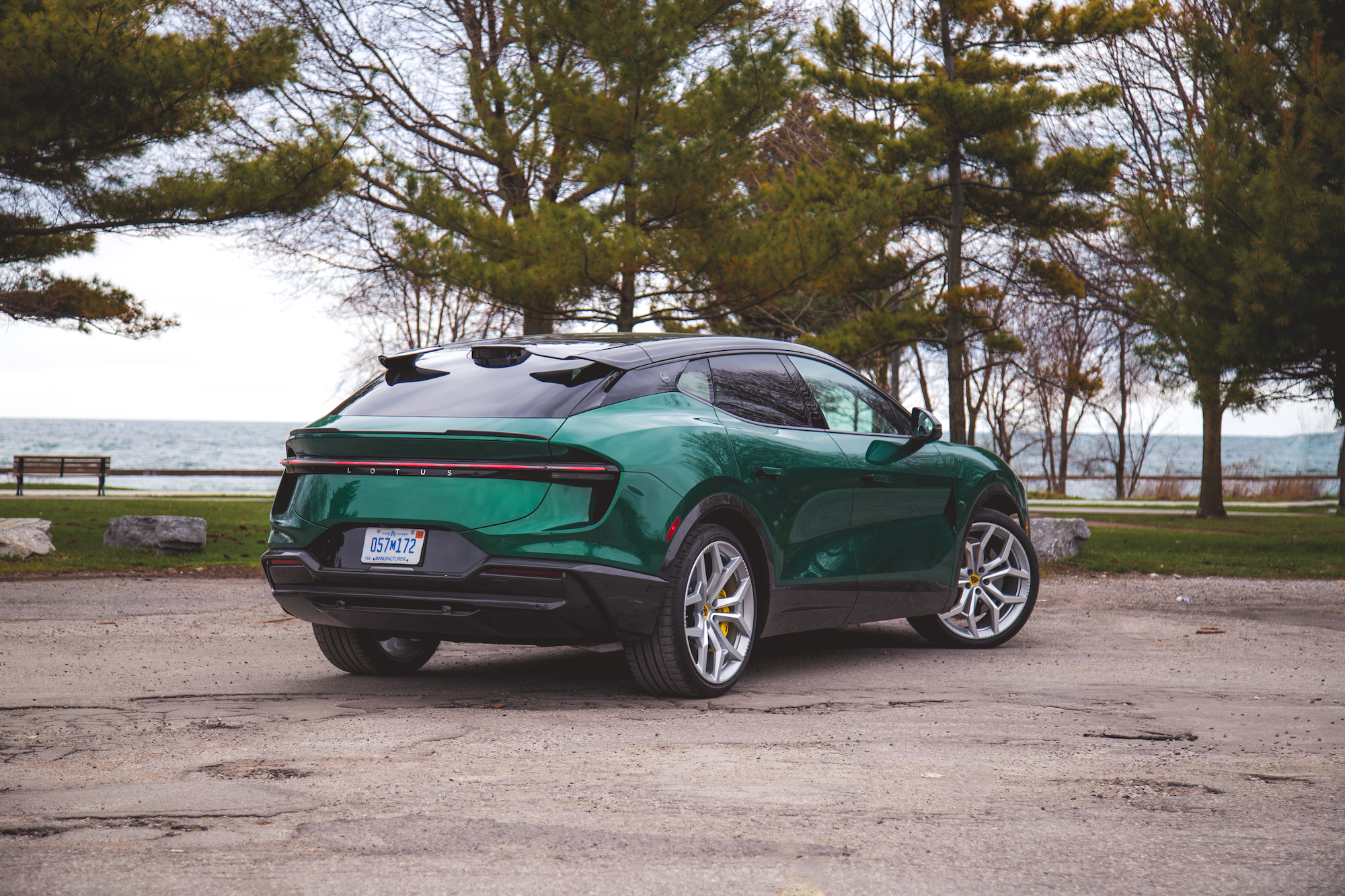 Vista trasera de un SUV eléctrico verde estacionado junto a un lago con árboles al fondo.