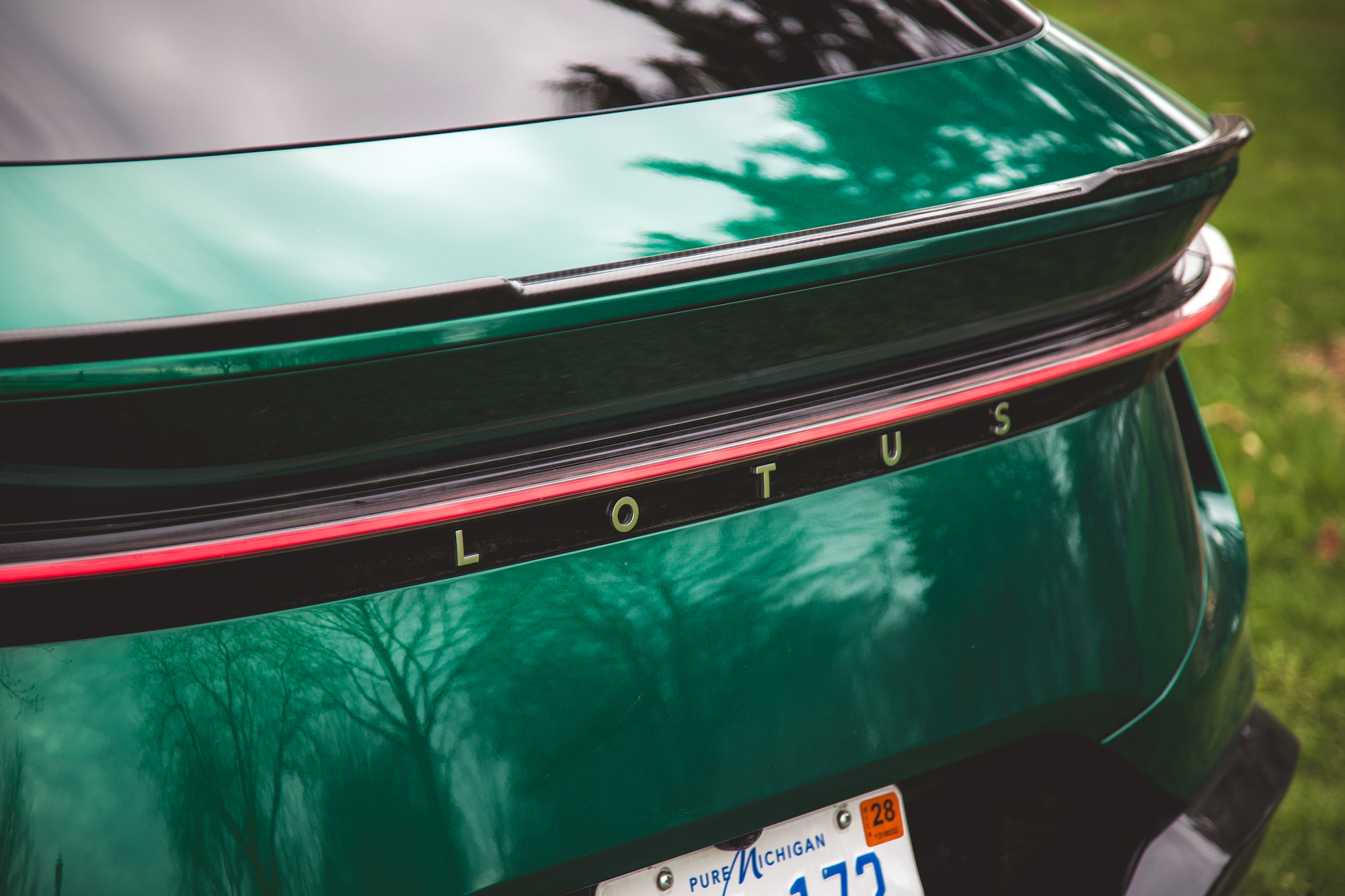 Primer plano de la parte trasera de un automóvil Lotus verde que muestra la marca 'LOTUS' en letras negras y una línea decorativa en rojo.