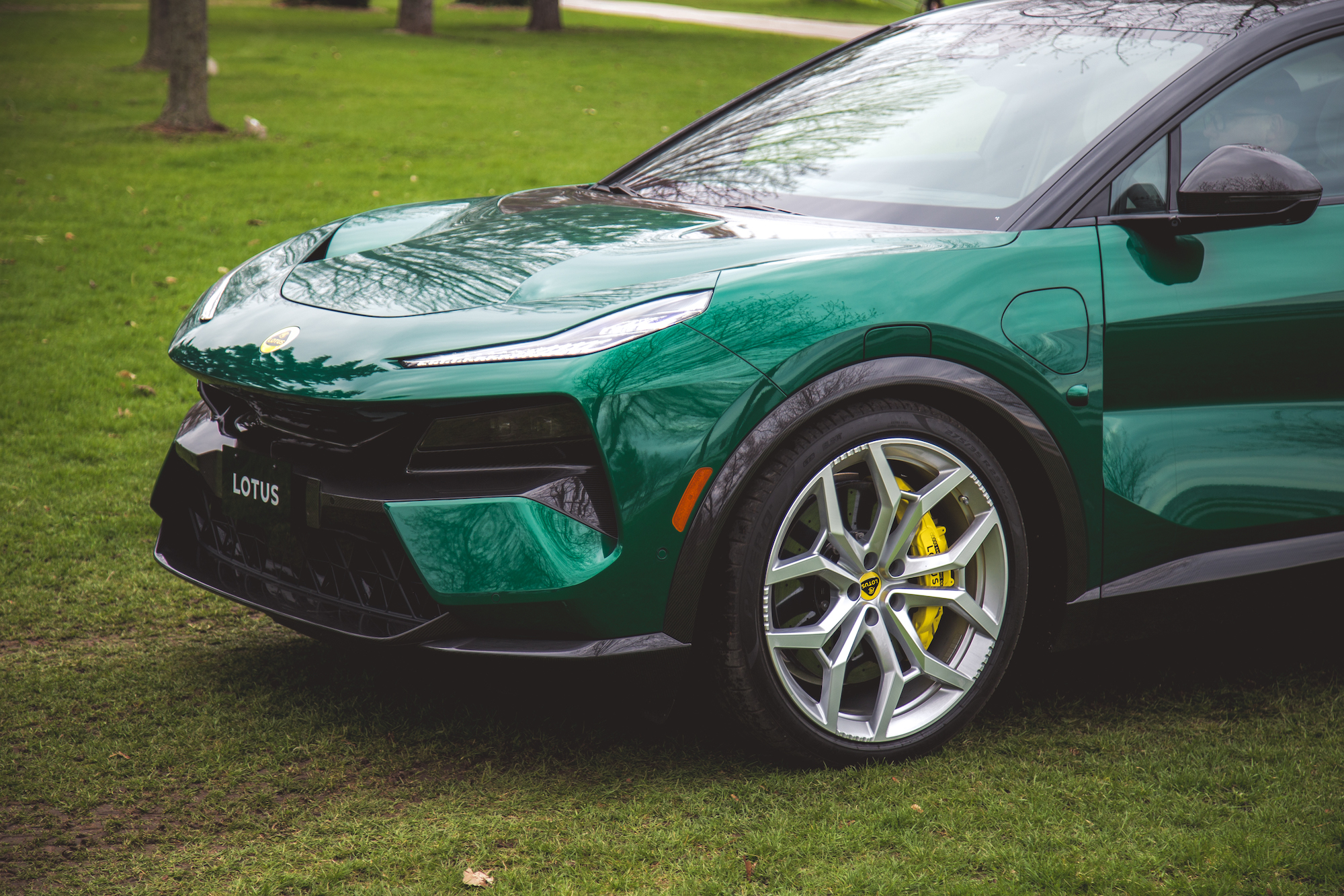 Vista cercana de un automóvil Lotus verde estacionado sobre el césped, que muestra su elegante diseño, su distintiva parrilla delantera y sus llantas de aleación con pinzas de freno amarillas.