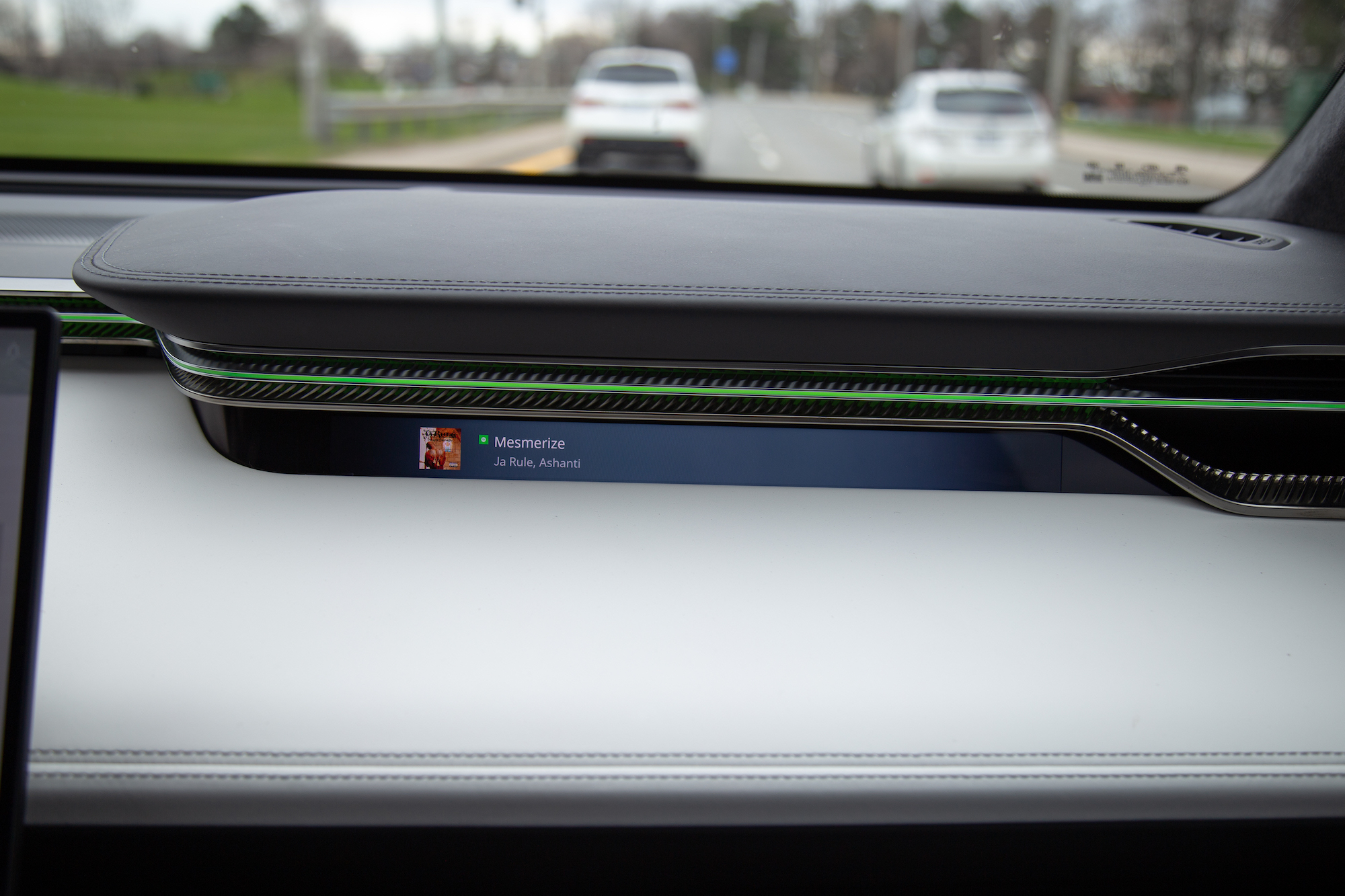 Vista interior del tablero de un automóvil que muestra una interfaz musical que muestra la canción 'Mesmerize' de Ja Rule con Ashanti.