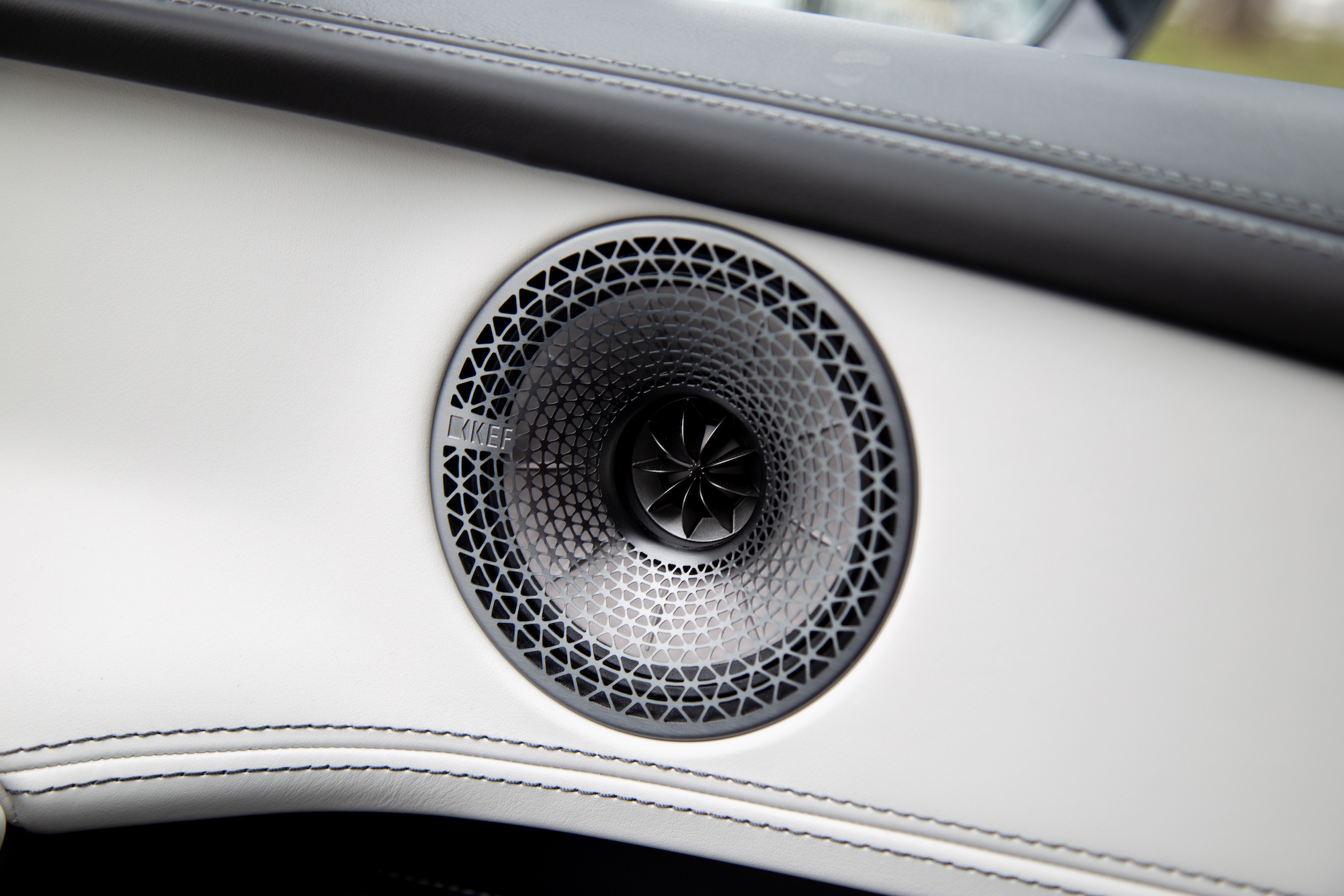 Vista cercana de un altavoz KEF integrado en el interior de un automóvil con un elegante diseño en blanco y negro.