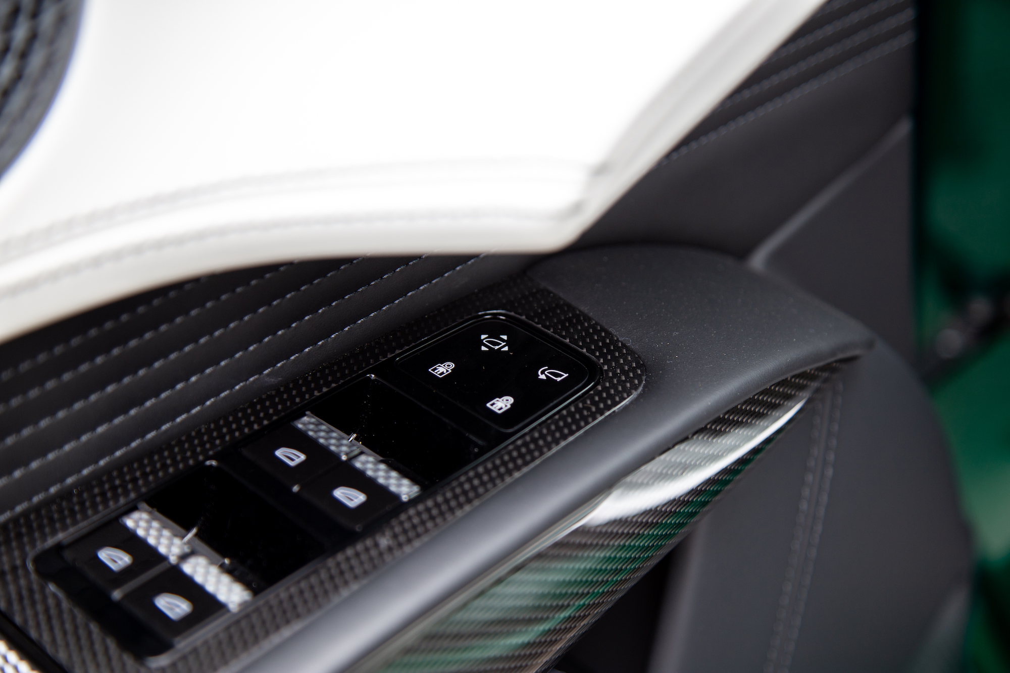 Primer plano del panel de la puerta de un automóvil con botones de control de ventanas y un diseño elegante y moderno con detalles en fibra de carbono.