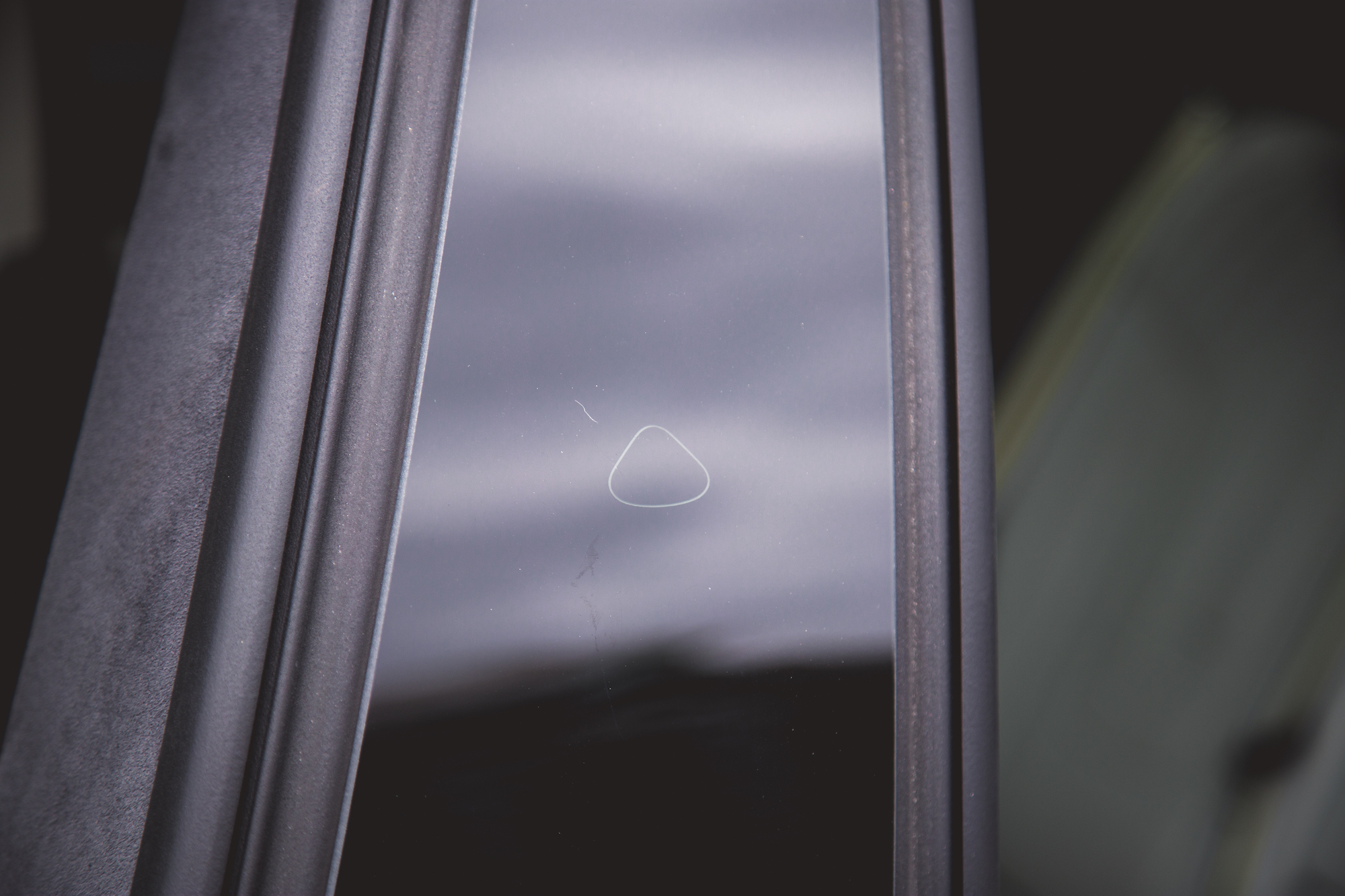 Primer plano de la ventanilla de un automóvil que muestra una pequeña marca triangular o rasguño en el vidrio, con un marco oscuro rodeándola.