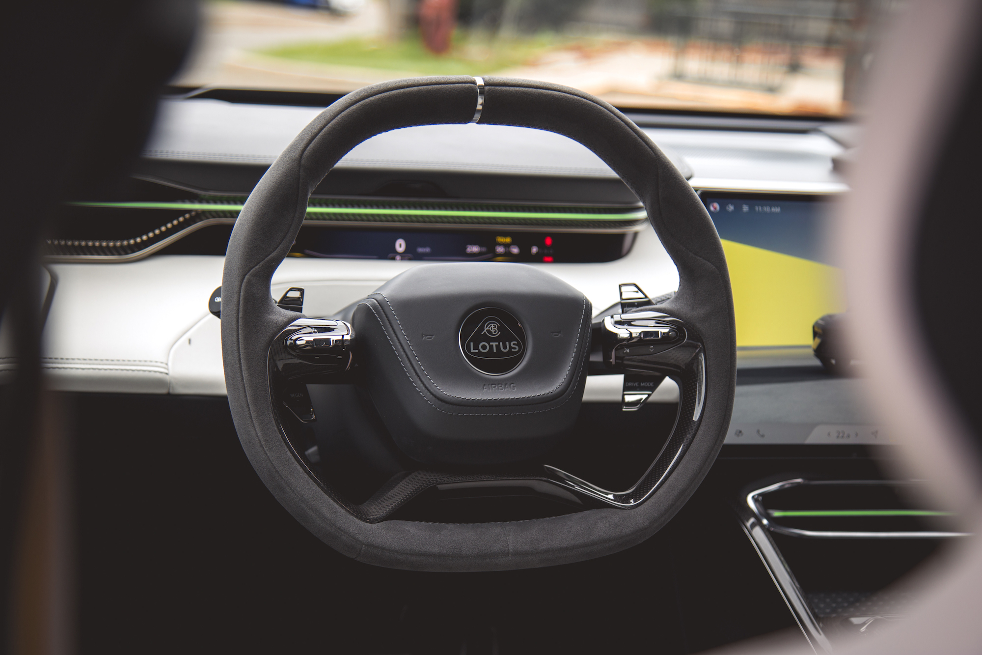 Primer plano del volante de un automóvil moderno con el logotipo de Lotus, un tablero elegante y una pantalla digital al fondo.