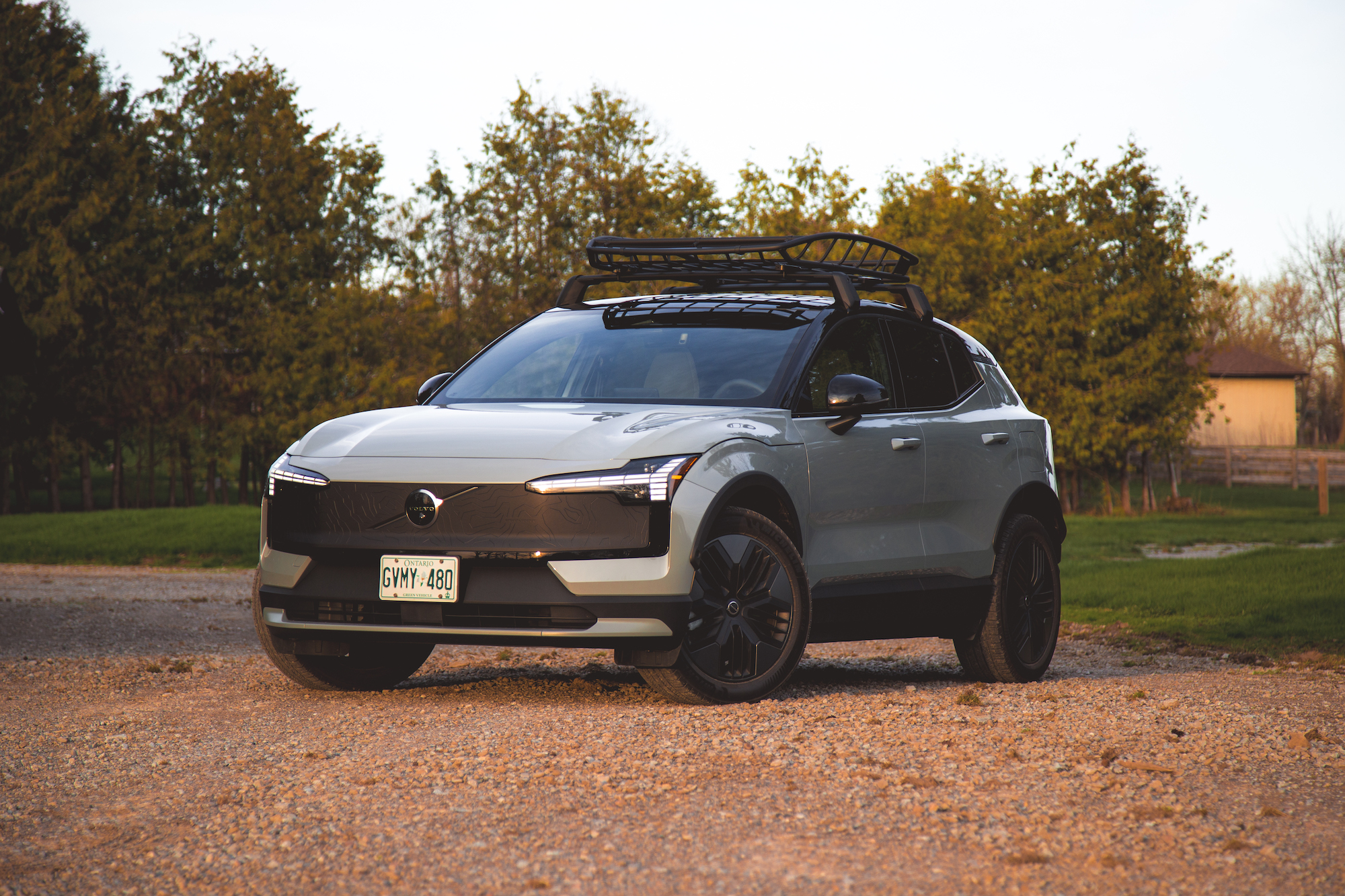 Un moderno SUV eléctrico Volvo estacionado sobre grava, con una baca negra y rodeado de vegetación.