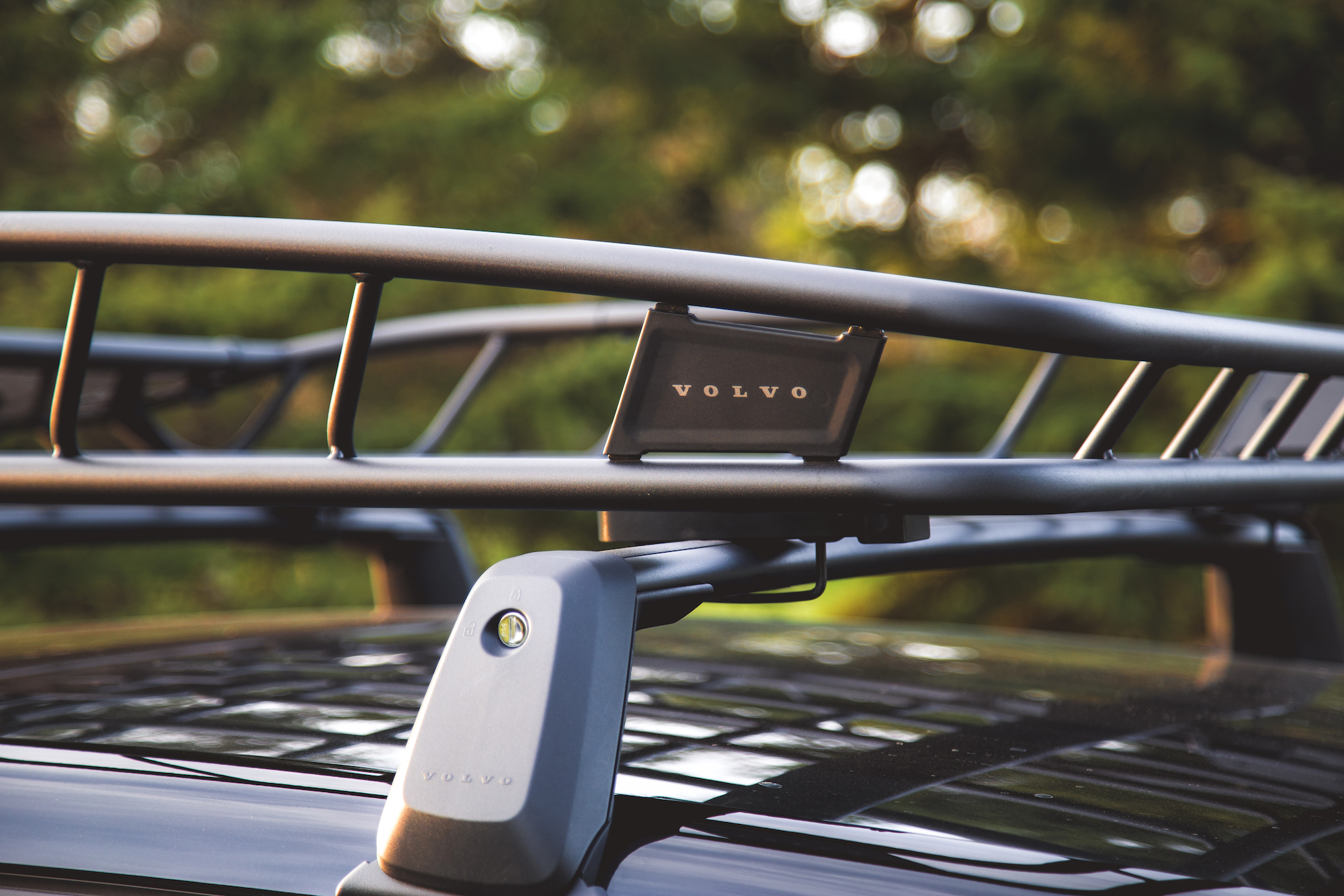 Primer plano de un accesorio de portaequipajes de techo Volvo en un vehículo con vegetación borrosa en el fondo.