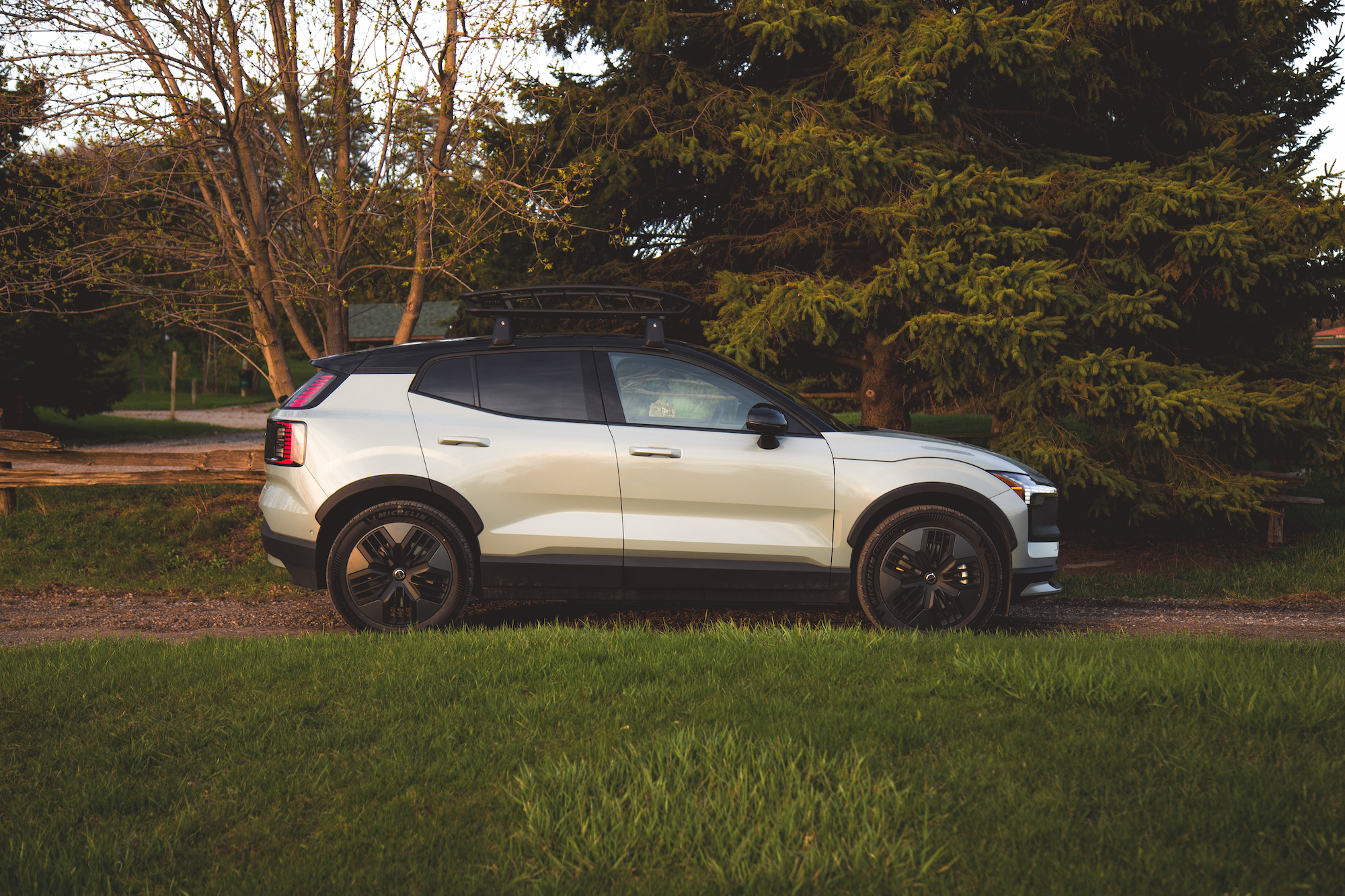 Una vista lateral de un SUV blanco estacionado en un camino de grava, rodeado de hierba verde y árboles.