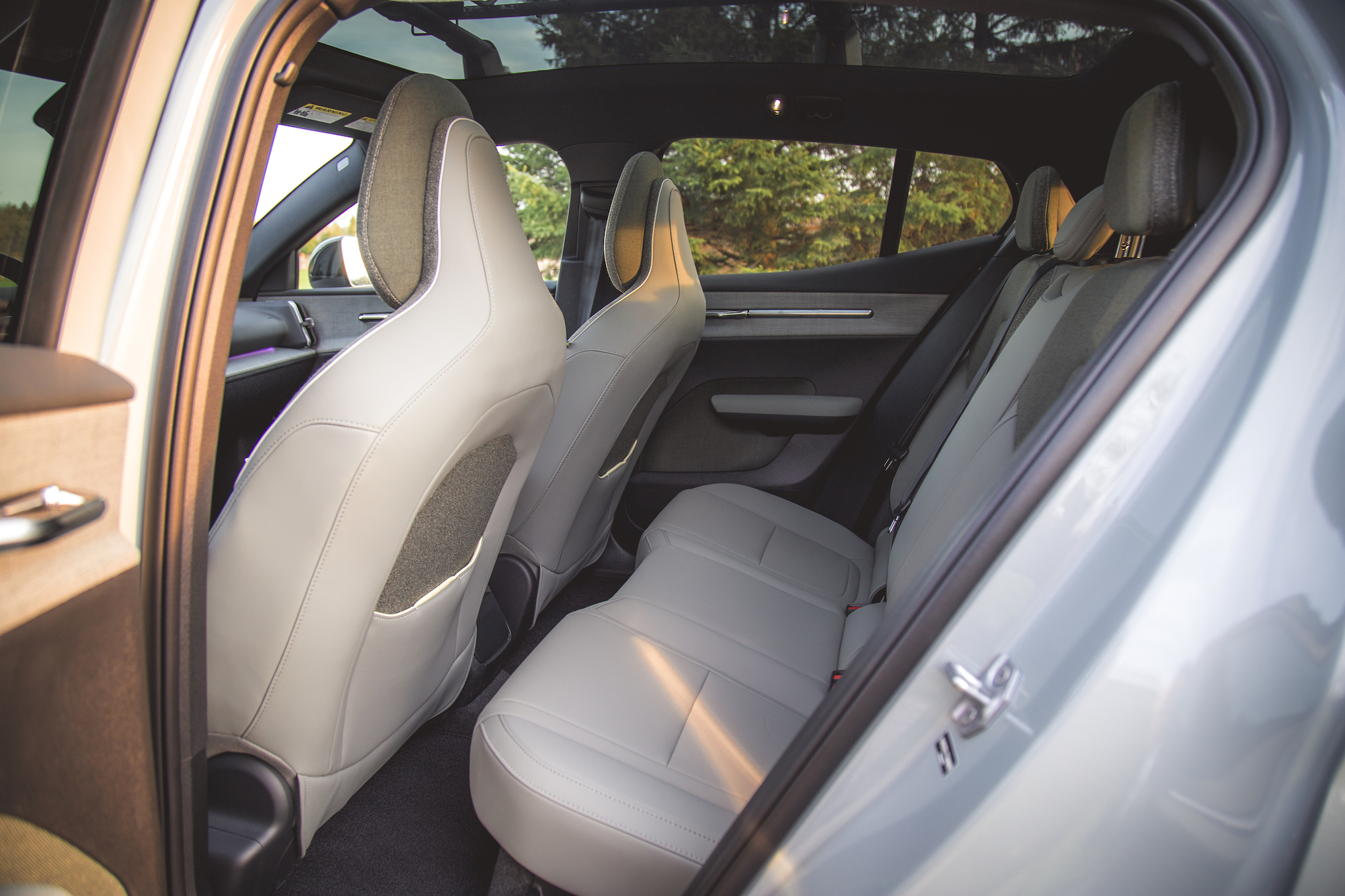 Vista interior del asiento trasero de un automóvil moderno, con dos asientos orientados hacia adelante con tapizado gris claro y techo panorámico.