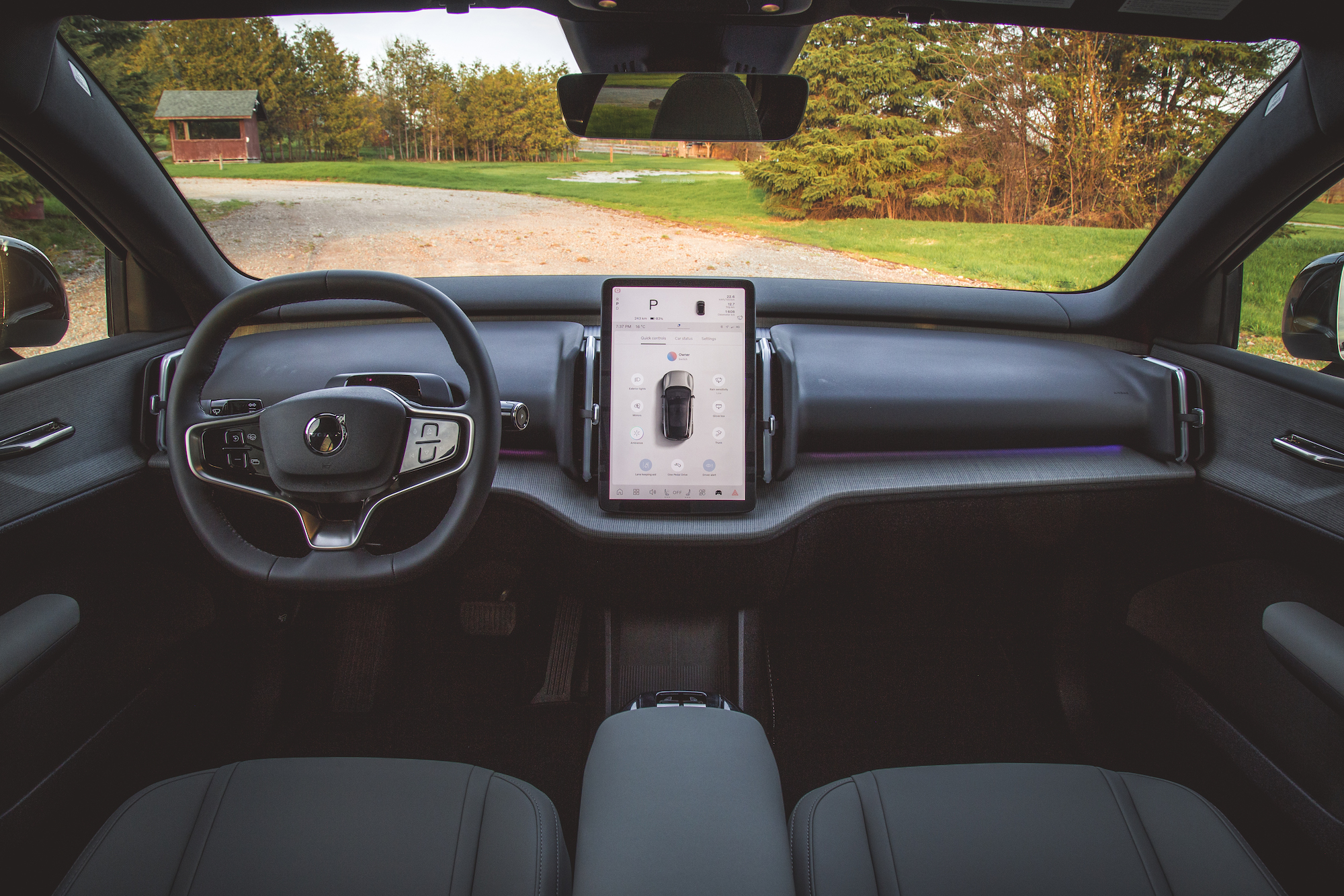 Vista interior de un vehículo eléctrico moderno con volante, pantalla táctil grande y un elegante diseño de tablero.