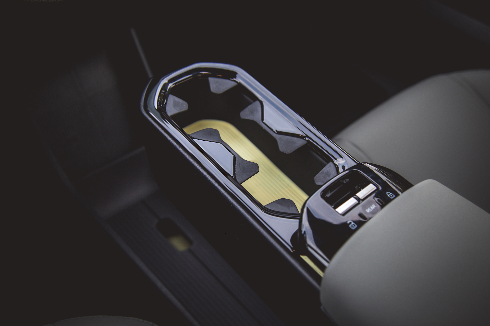 Primer plano de la consola central de un automóvil, que presenta un diseño elegante con un acabado brillante y una incrustación de madera.