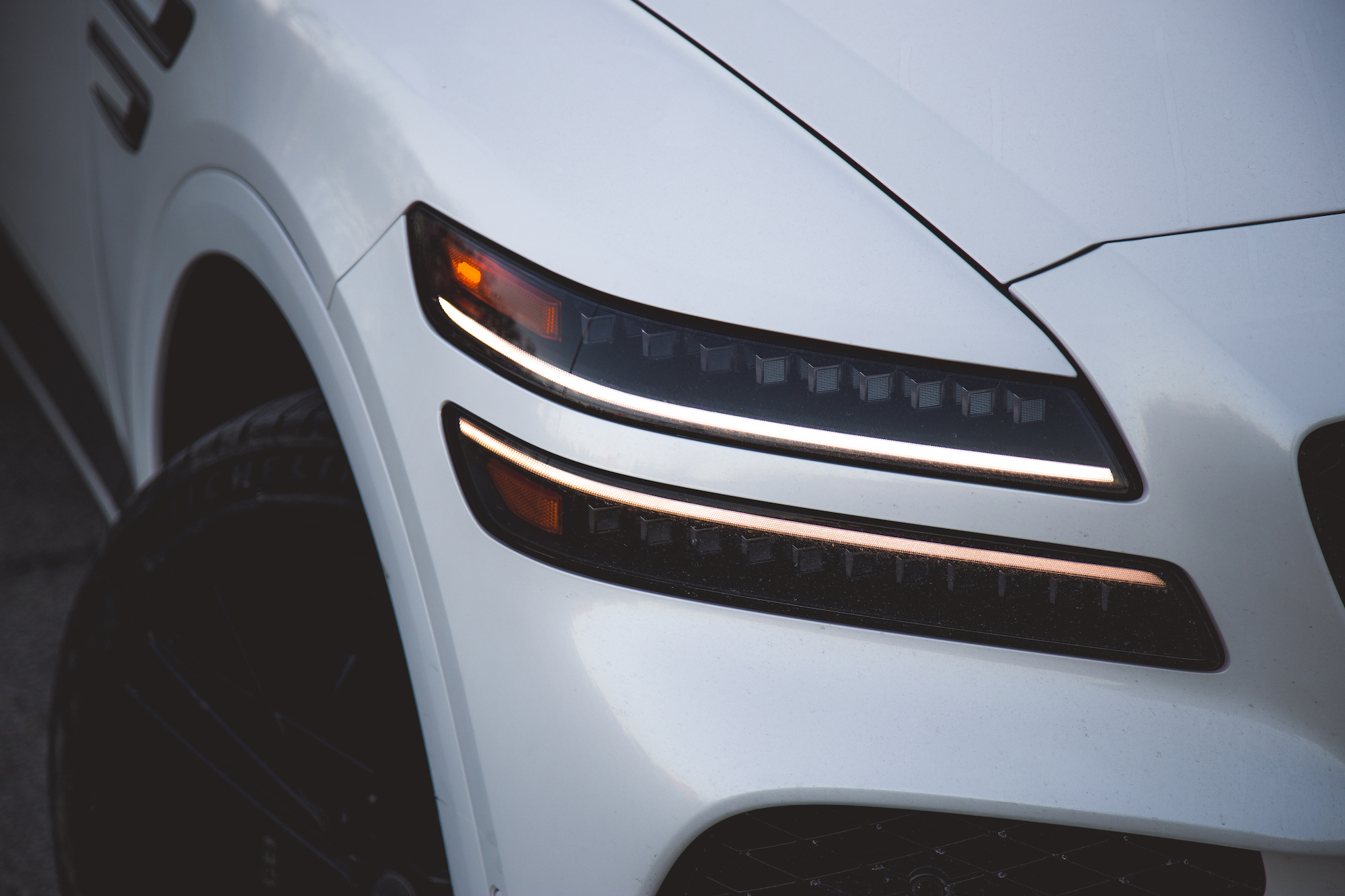 Close-up of the headlight and front fender of a white luxury SUV, showcasing sleek design elements and modern lighting.