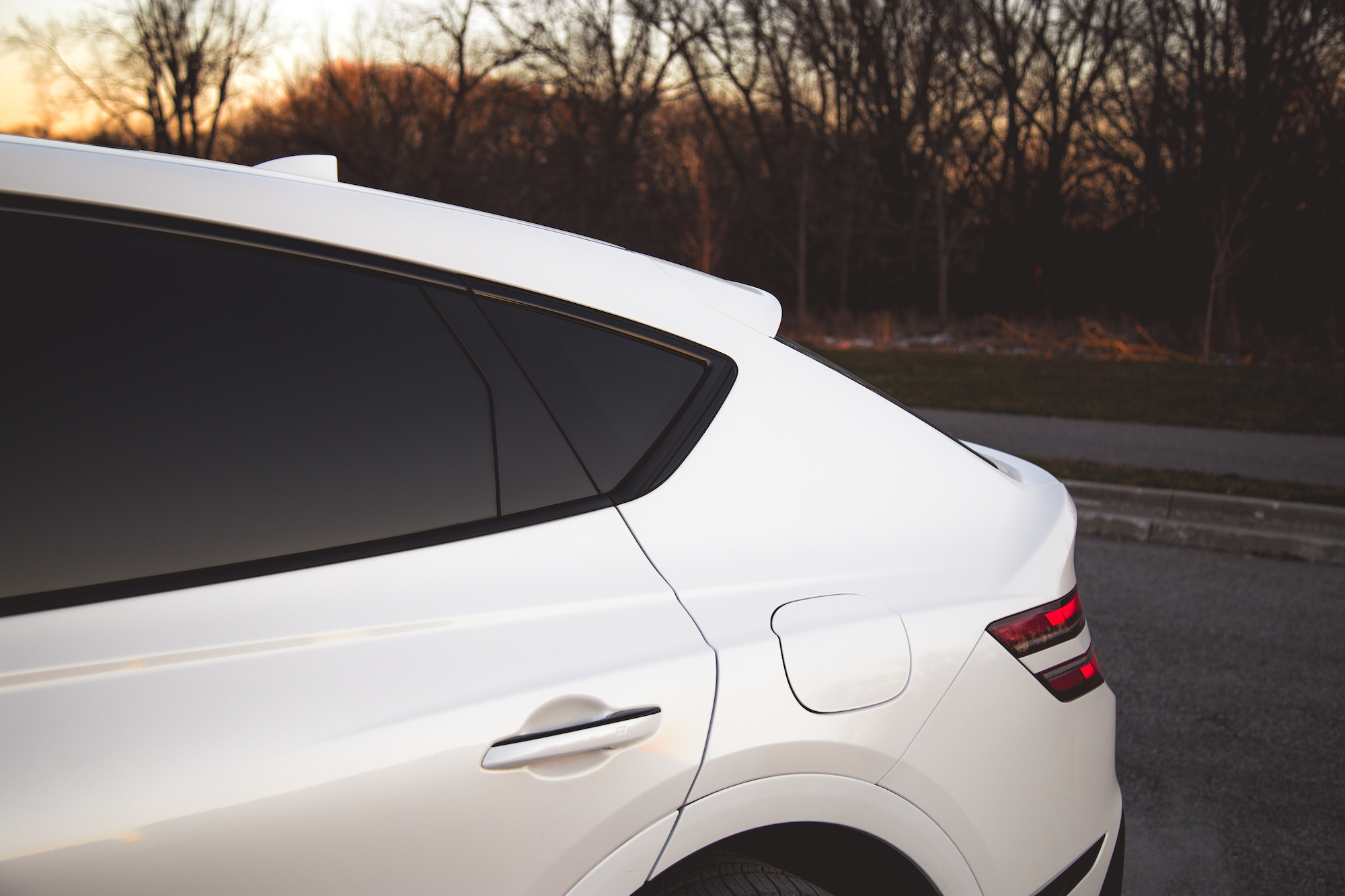 Close-up of the rear side of a white SUV with tinted windows, showcasing the roofline, spoiler, and fuel cap.