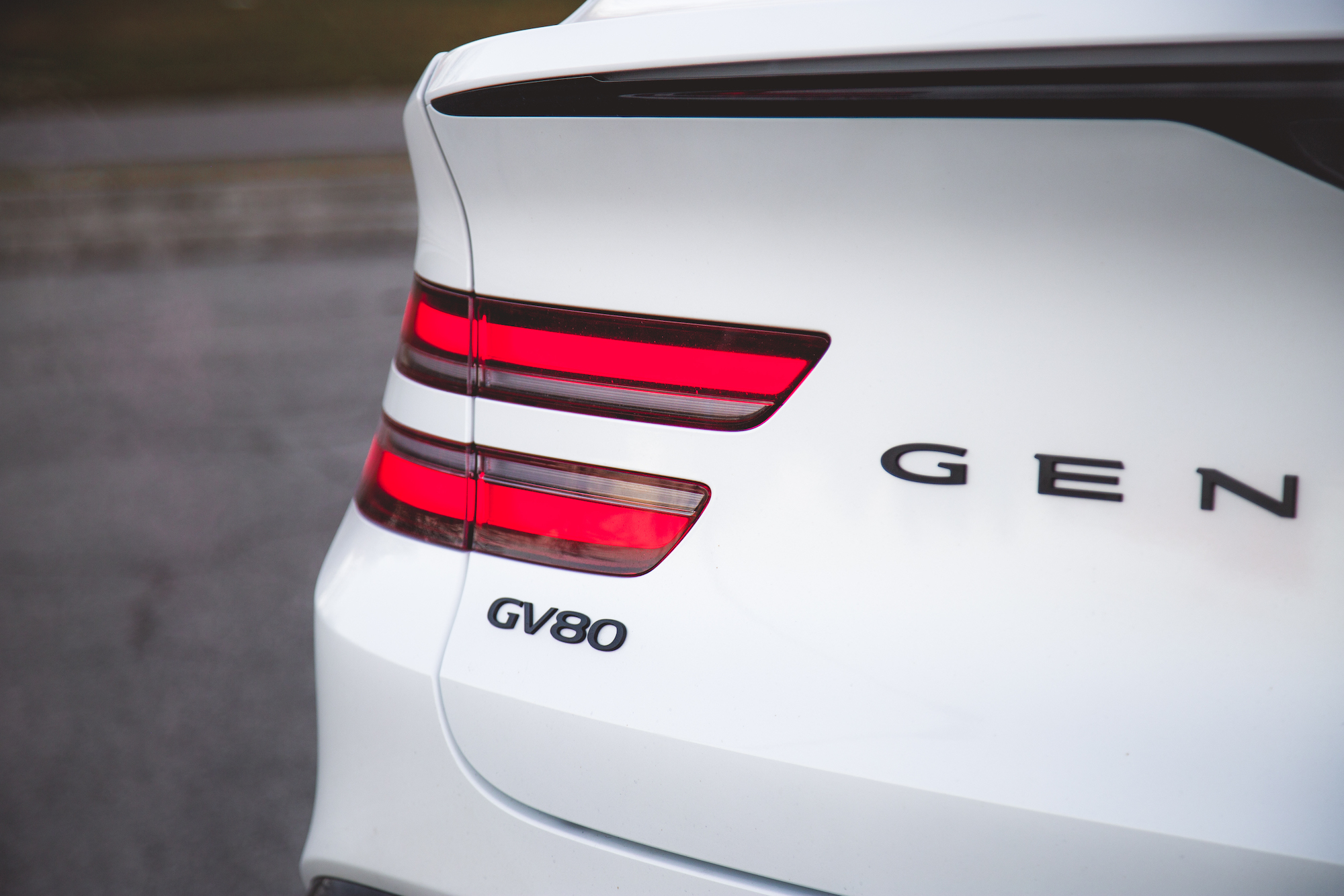 Close-up of the rear of a white Genesis GV80 luxury SUV, showcasing the sleek tail lights and the Genesis logo.