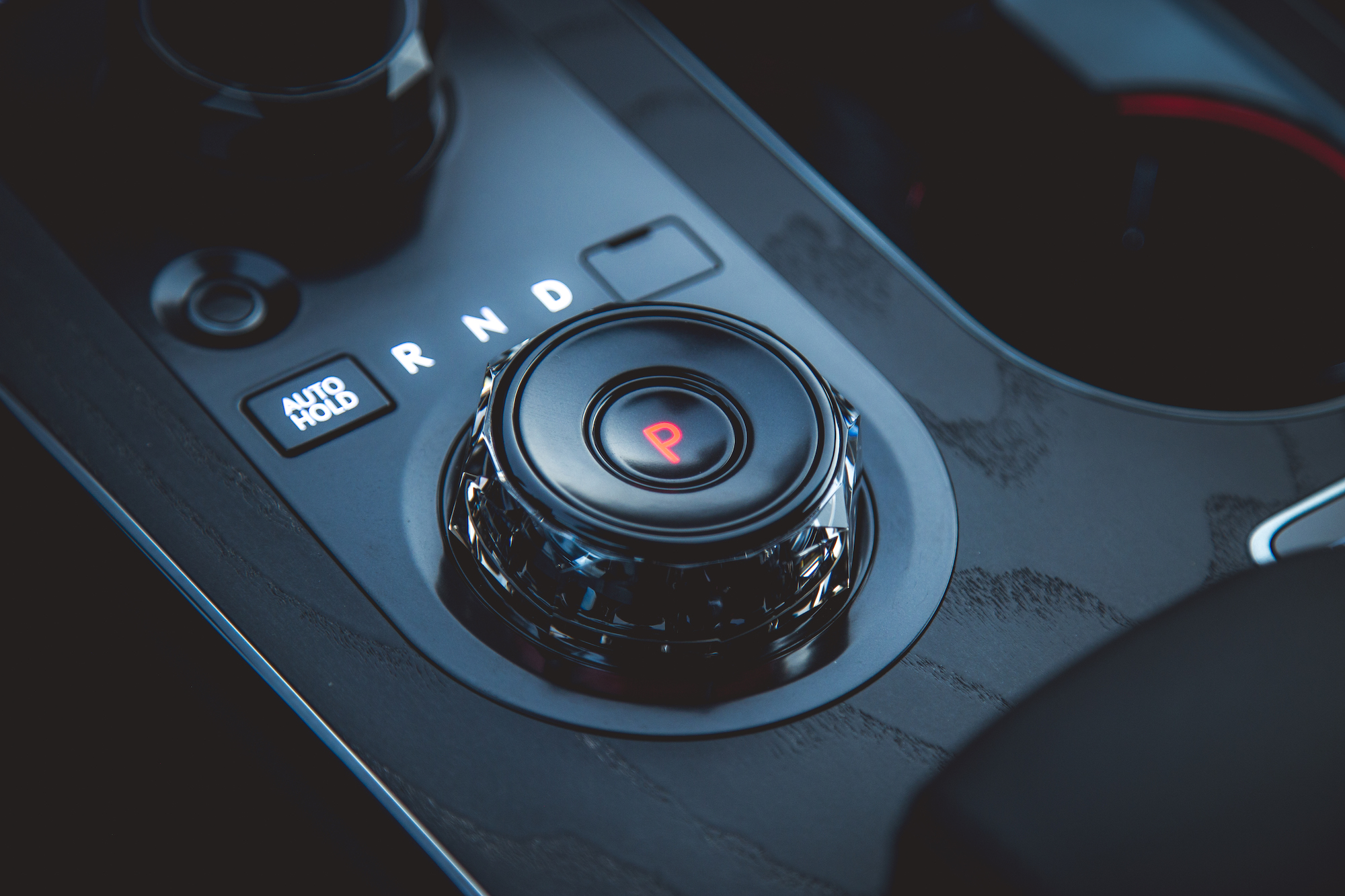 Close-up of a car's gear shift with a circular knob labeled 'P' for parking, surrounded by controls for 'R' (reverse), 'N' (neutral), and 'D' (drive), featuring a sleek black interior.