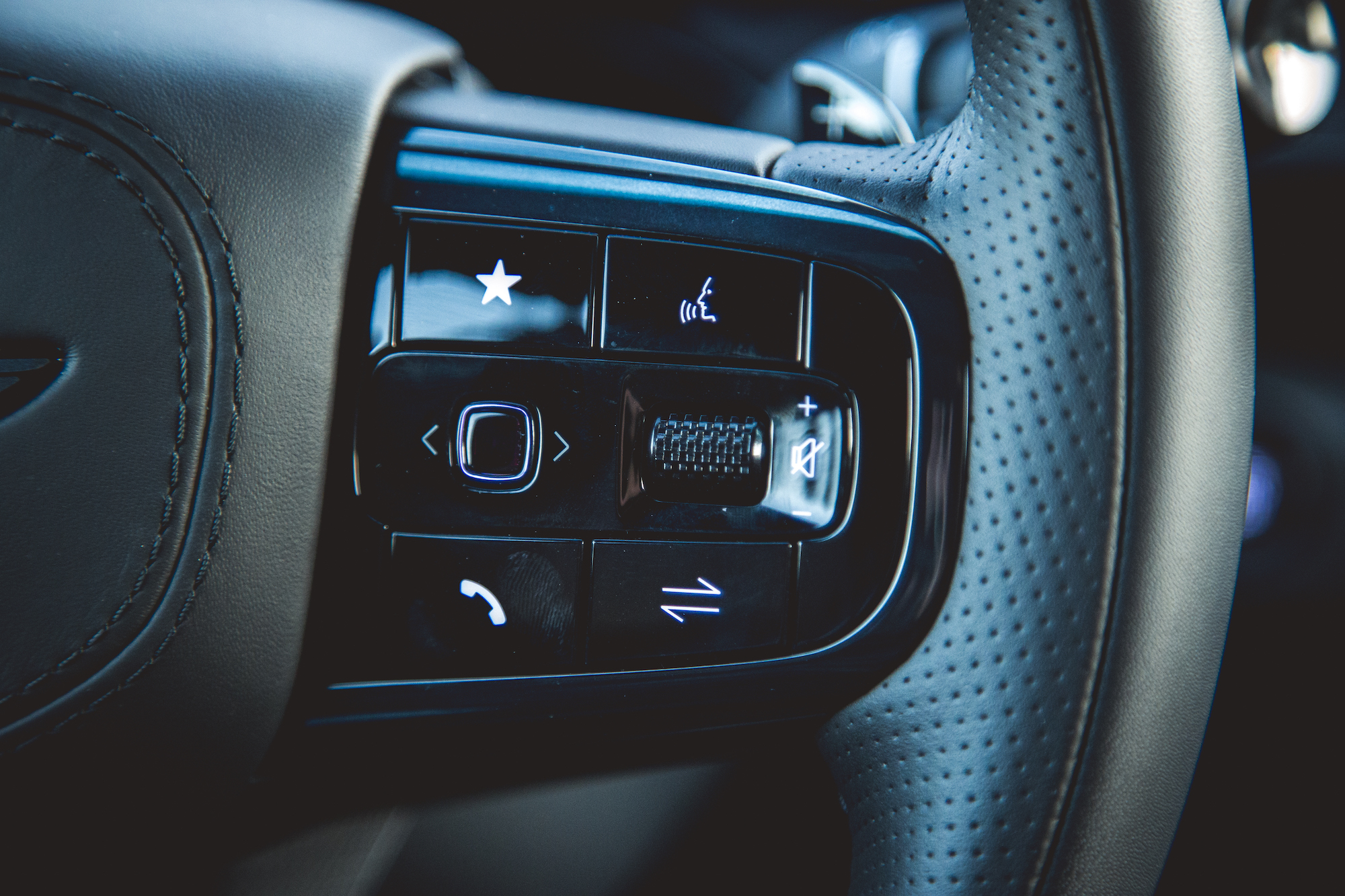 Close-up of a car steering wheel control panel featuring buttons for calls, audio, and settings.