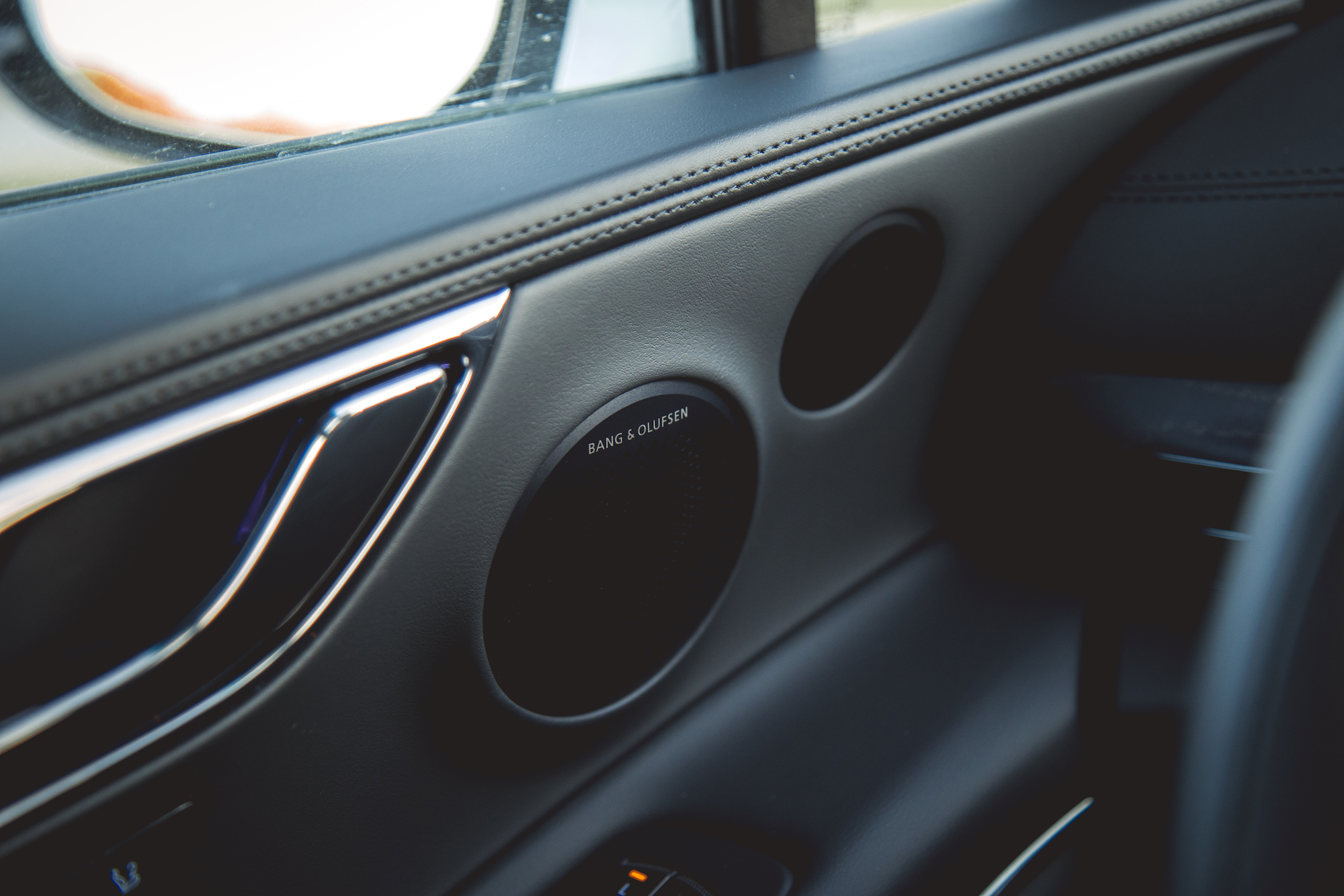 Close-up view of luxury car interior featuring a Bang & Olufsen speaker with stylish metallic trim and soft-touch materials.