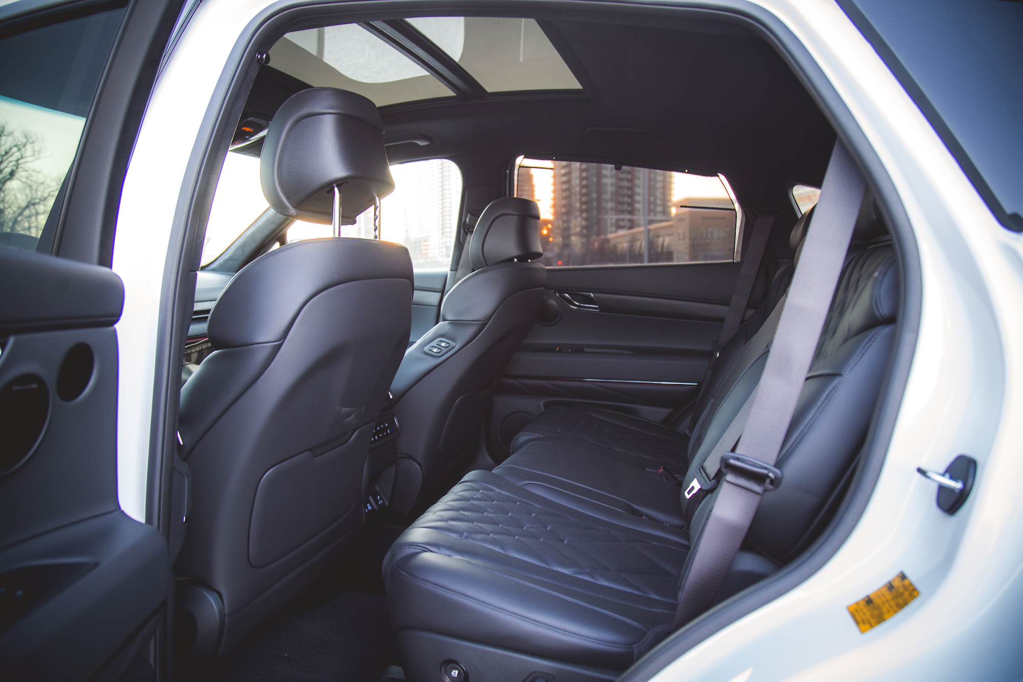 Interior view of a luxury car's back seat, featuring leather upholstery, a panoramic sunroof, and a spacious design.