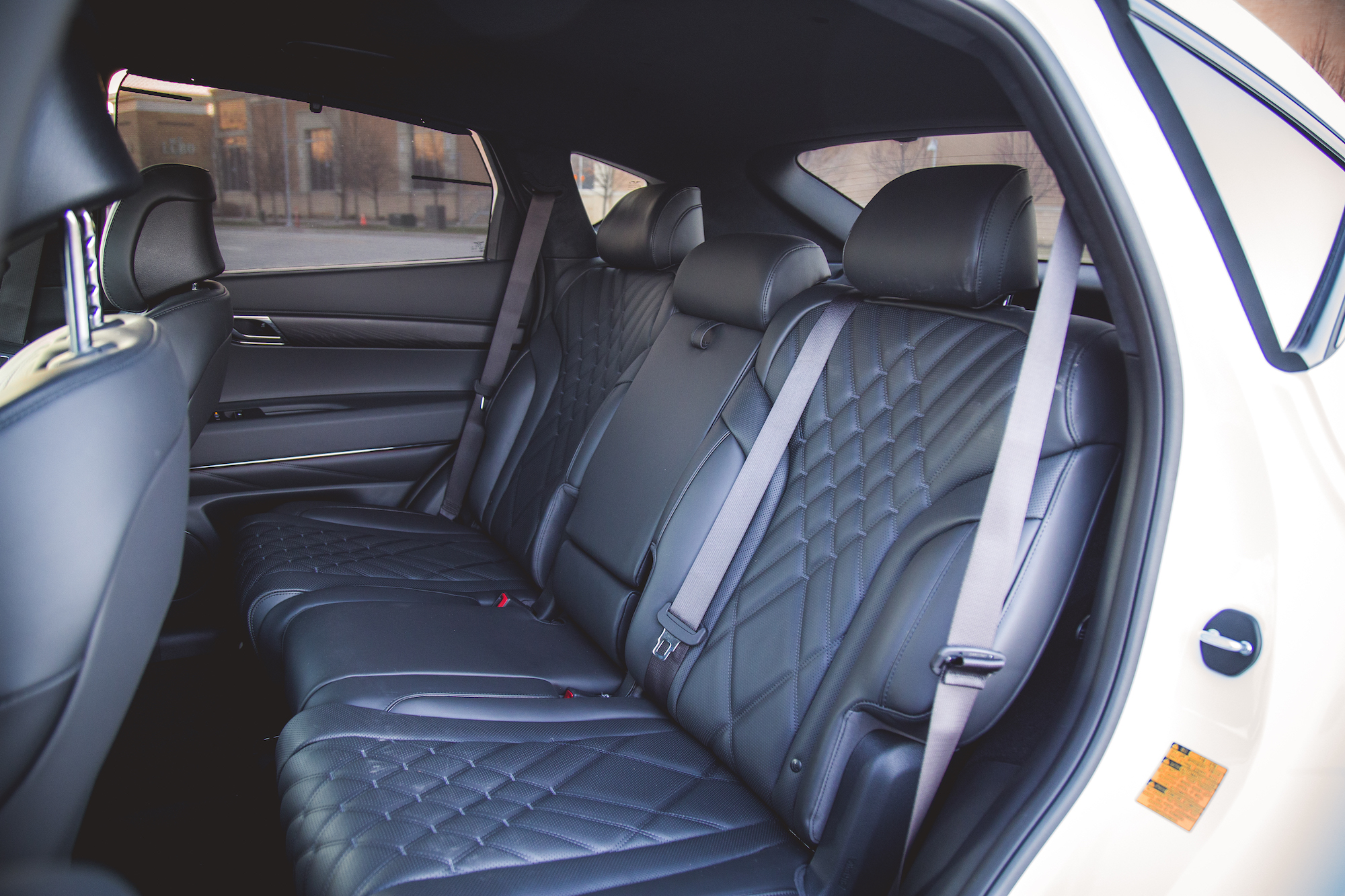 Interior view of a car showing the black leather backseat with quilted detailing and seat belts.