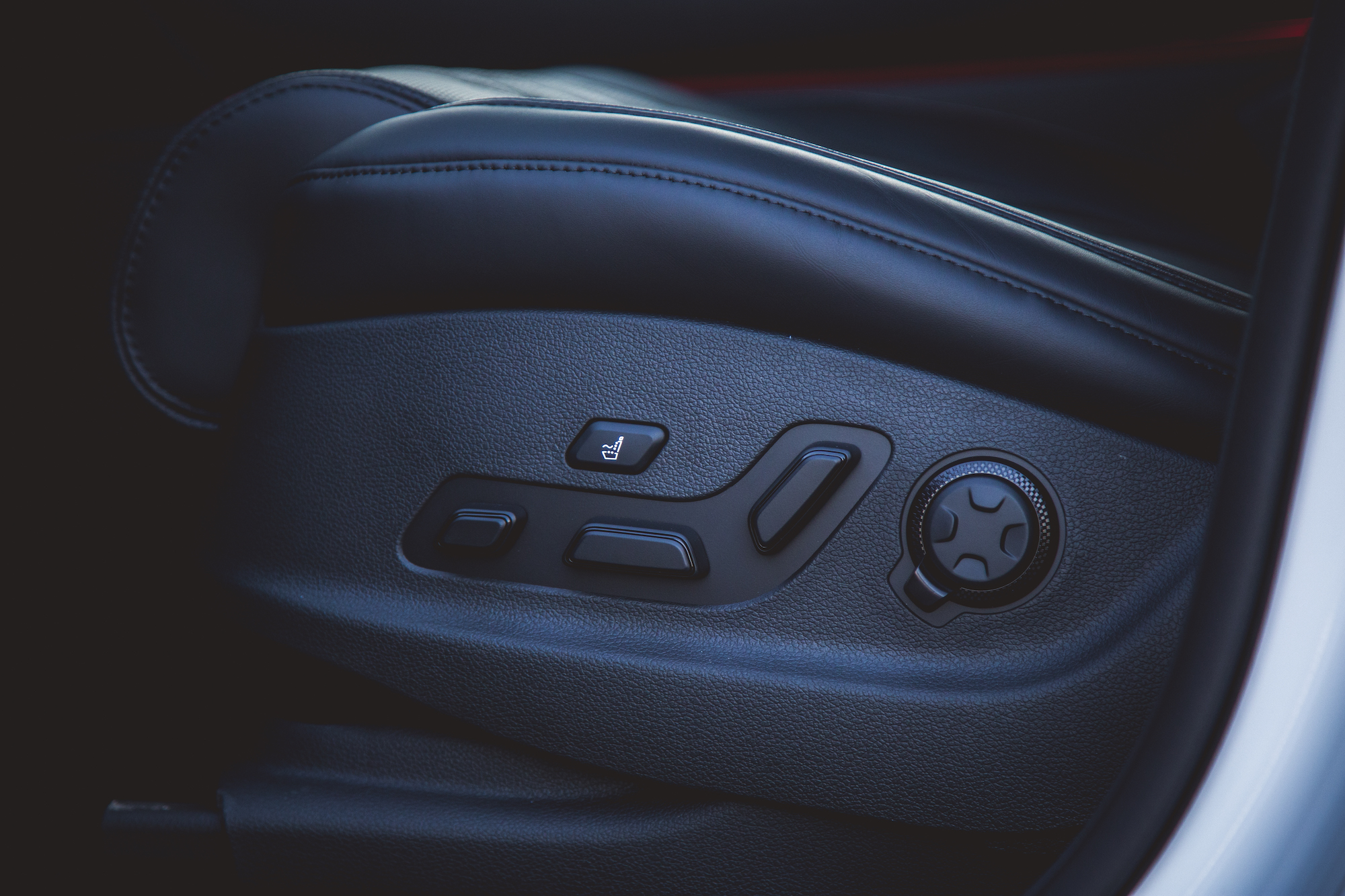 Close-up of a car seat control panel featuring buttons for adjusting seat position and a dial for lumbar support.