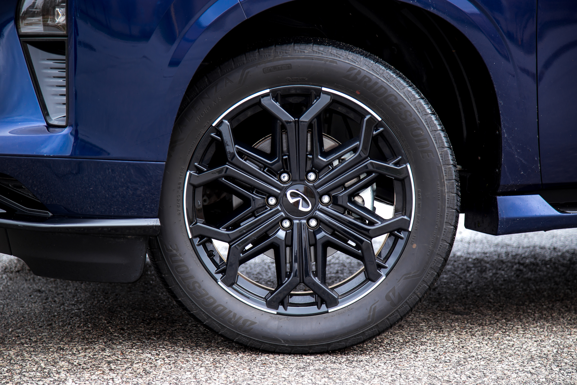 Primer plano de una elegante llanta de aleación negra en un vehículo azul con neumático Bridgestone.