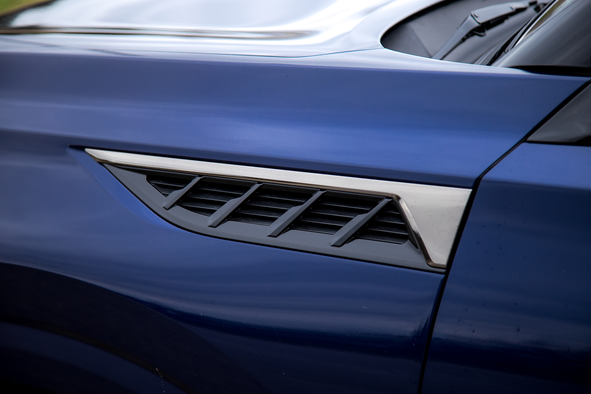 Primer plano del panel lateral de un automóvil azul con una elegante salida de aire con adornos decorativos.