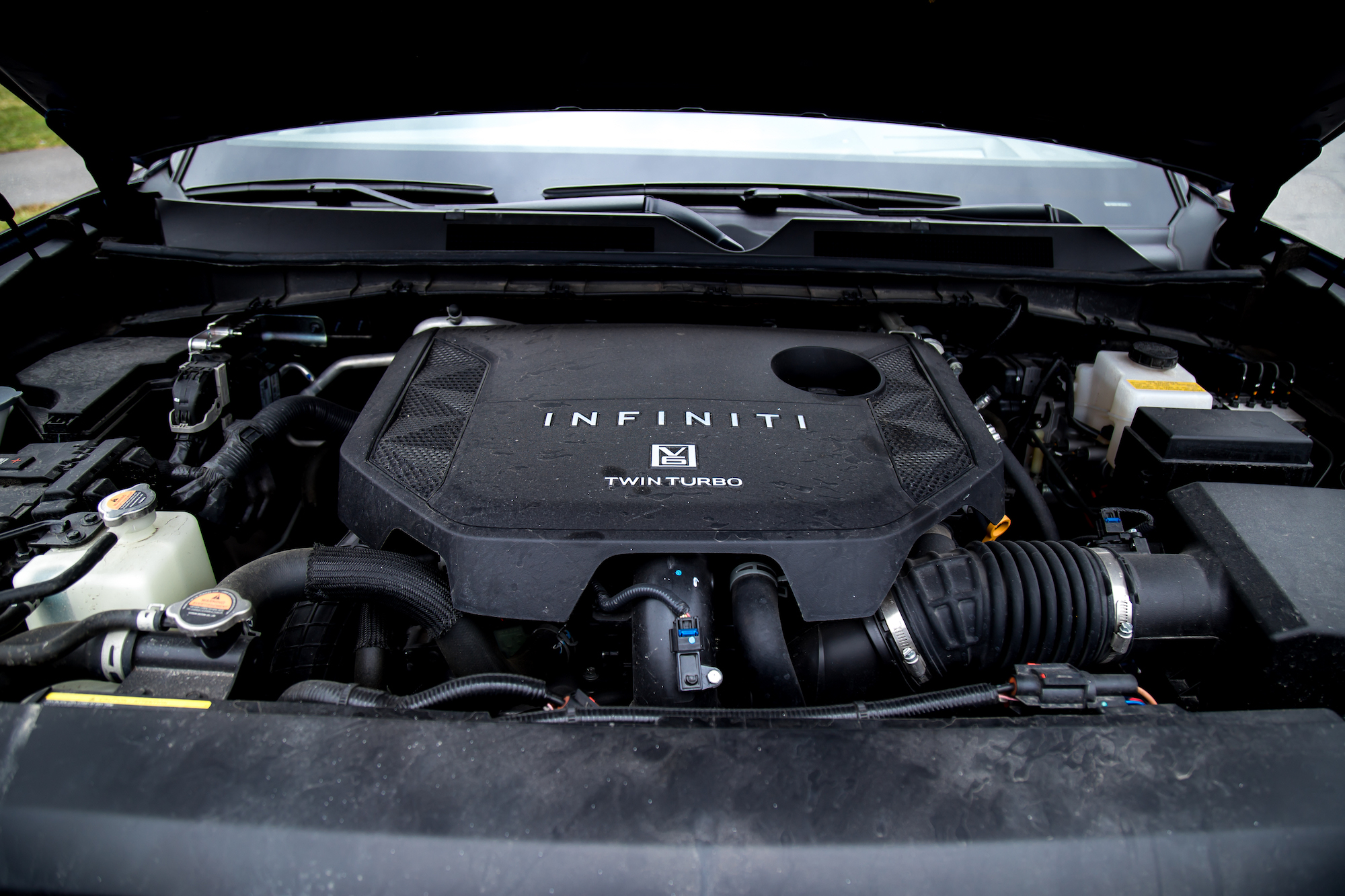 Vista del compartimiento del motor de un vehículo Infiniti que muestra la cubierta del motor biturbo y varios componentes.