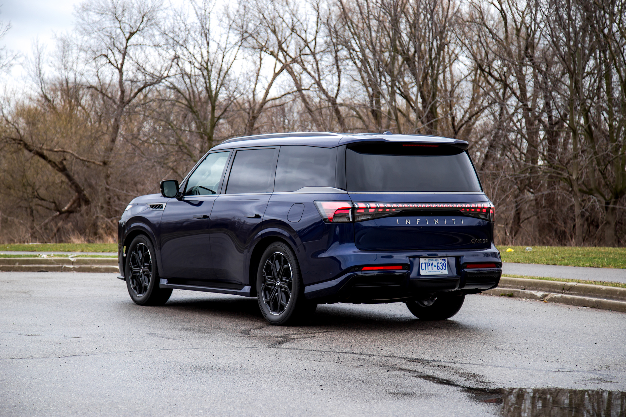 Un SUV Infiniti azul estacionado en una carretera circular con un fondo de árboles desnudos.