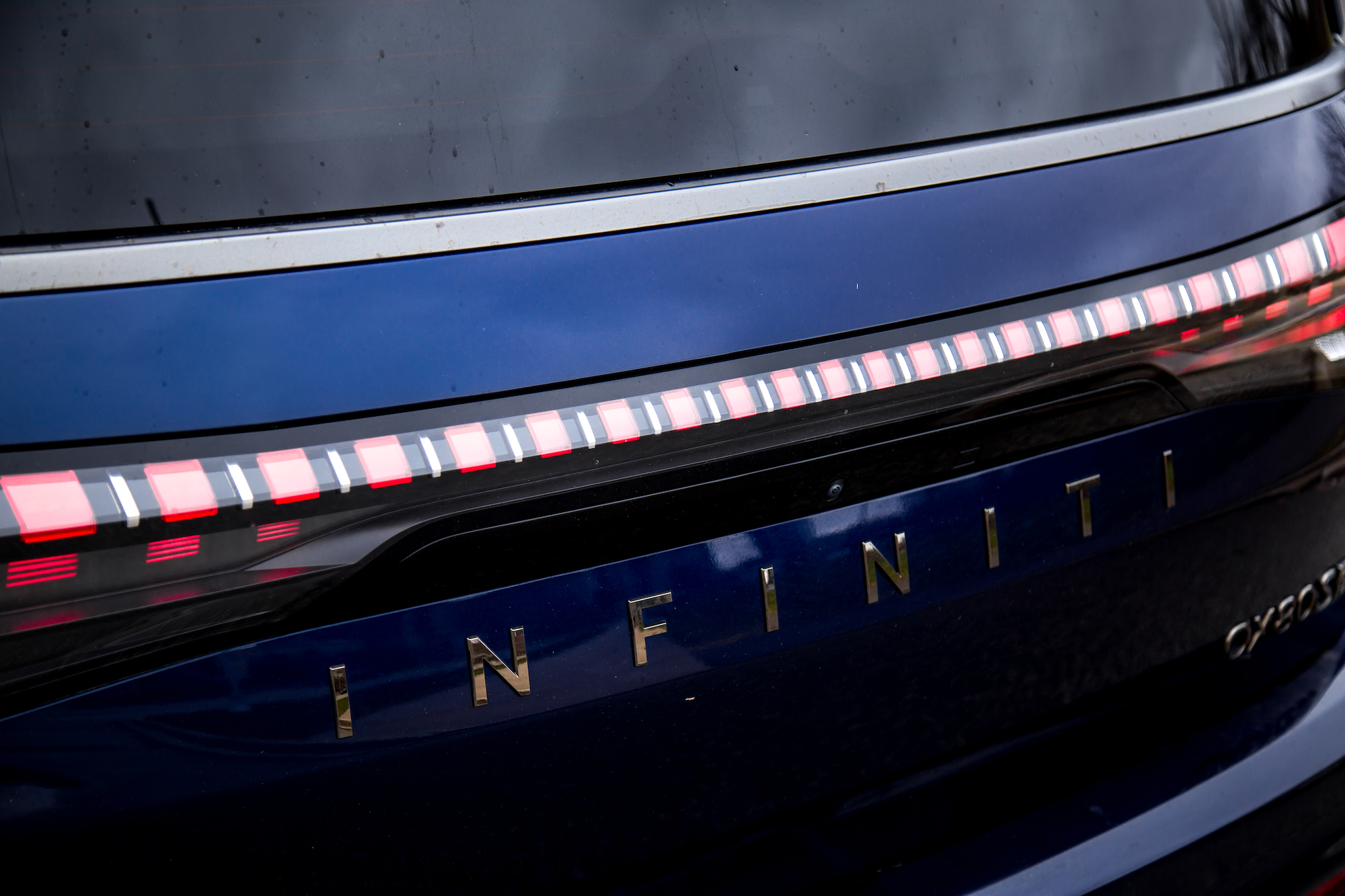 Primer plano de la parte trasera de un vehículo Infiniti azul, destacando las luces de freno iluminadas y el nombre de la marca.