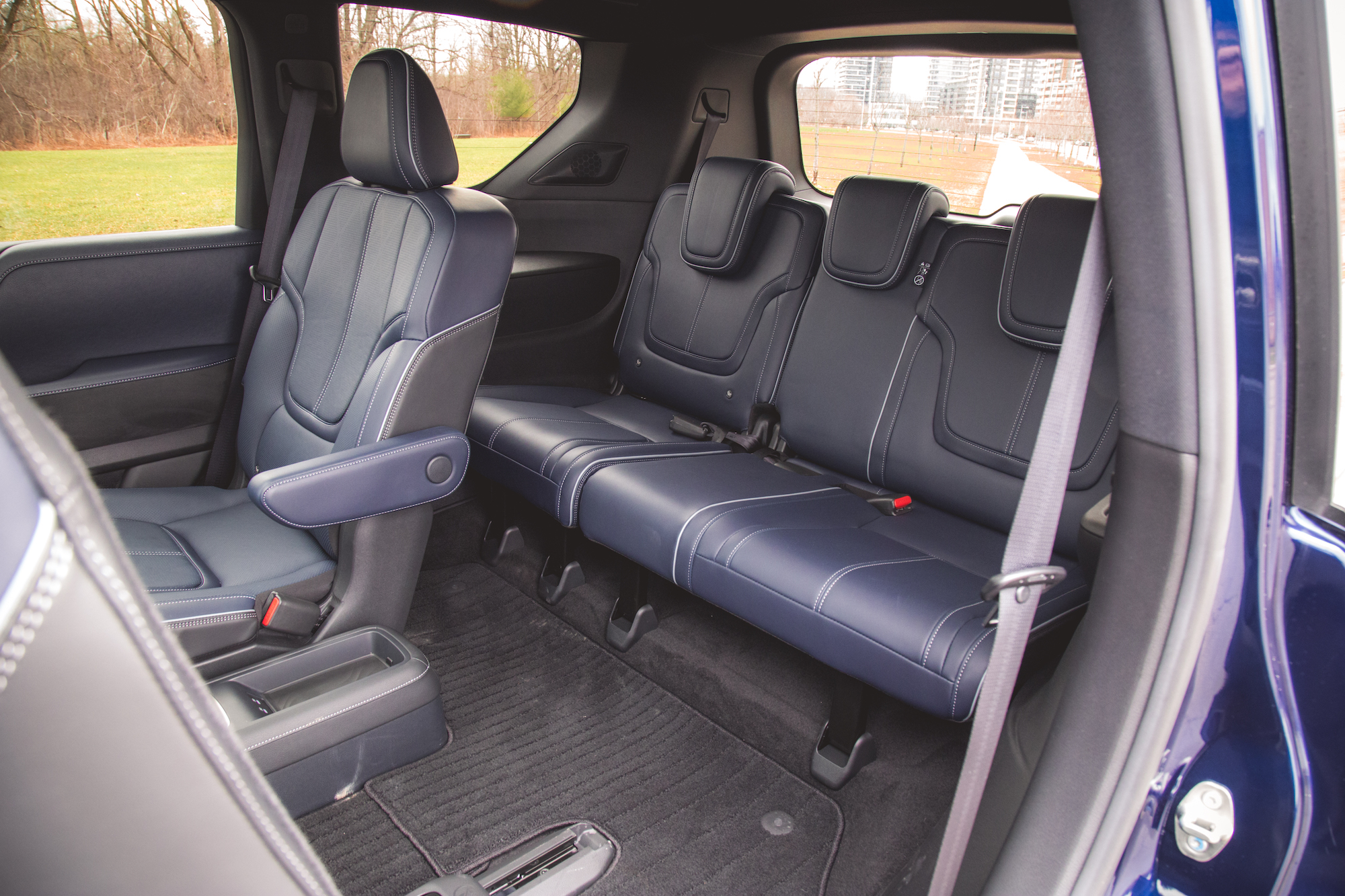 Vista interior de una espaciosa cabina con asientos de cuero azul marino, incluido un asiento del conductor con reposabrazos y un banco trasero. El suelo está alfombrado y al fondo se ve un paisaje de parque a través de la ventana.