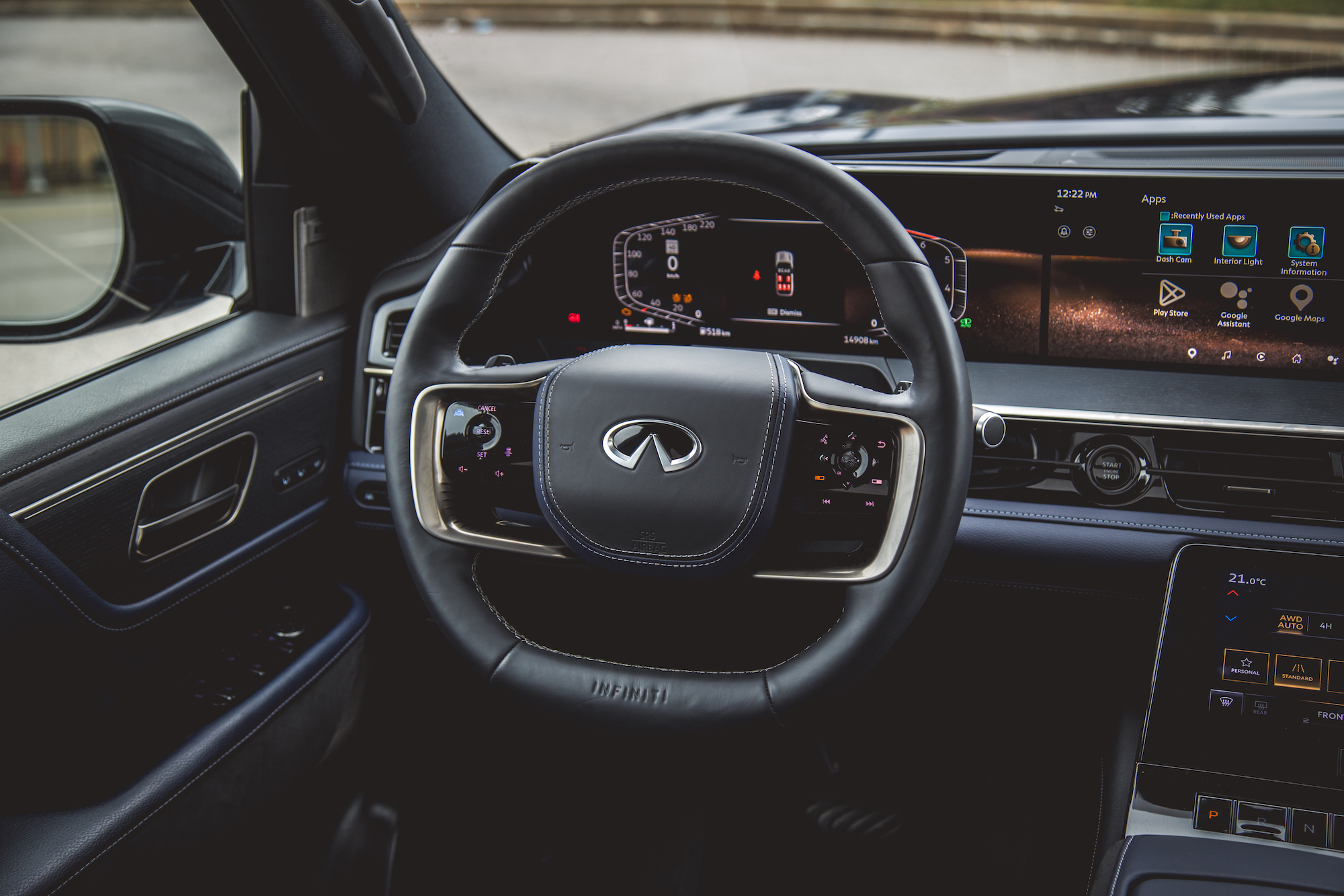 Vista interior del tablero de un automóvil de lujo, que presenta un volante con el logo Infinity, un panel de visualización digital con varios controles y una interfaz de pantalla táctil.