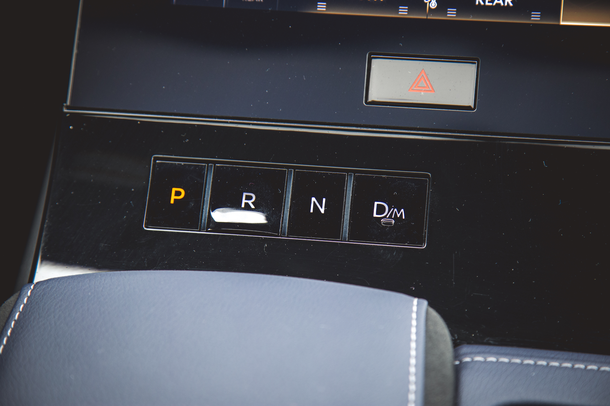 Vista de primer plano del panel de cambios de un automóvil, que muestra los botones de Estacionamiento (P), Marcha atrás (R), Neutral (N), Conducción (D) y Modo de conducción (D/M), junto con un botón de luz de emergencia.
