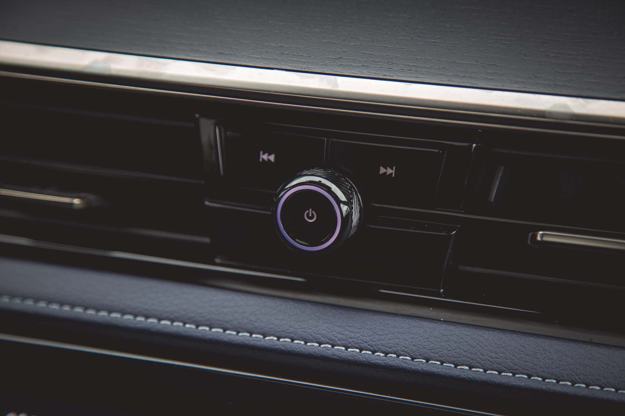 Primer plano de un panel de control de audio para automóvil con un botón de encendido redondo y controles de reproducción/pausa, sobre un fondo oscuro y texturizado.