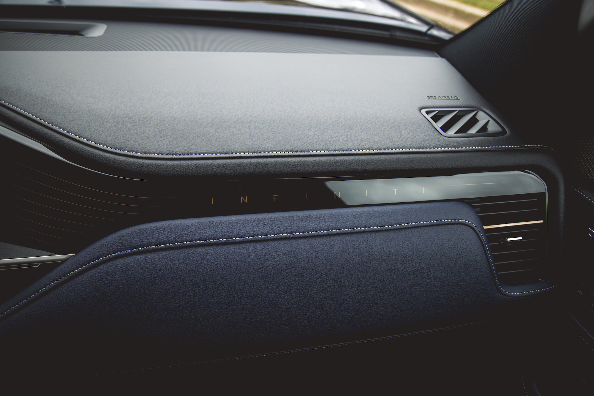 Primer plano del tablero de un automóvil de lujo con detalles en cuero y una salida de aire con la palabra 