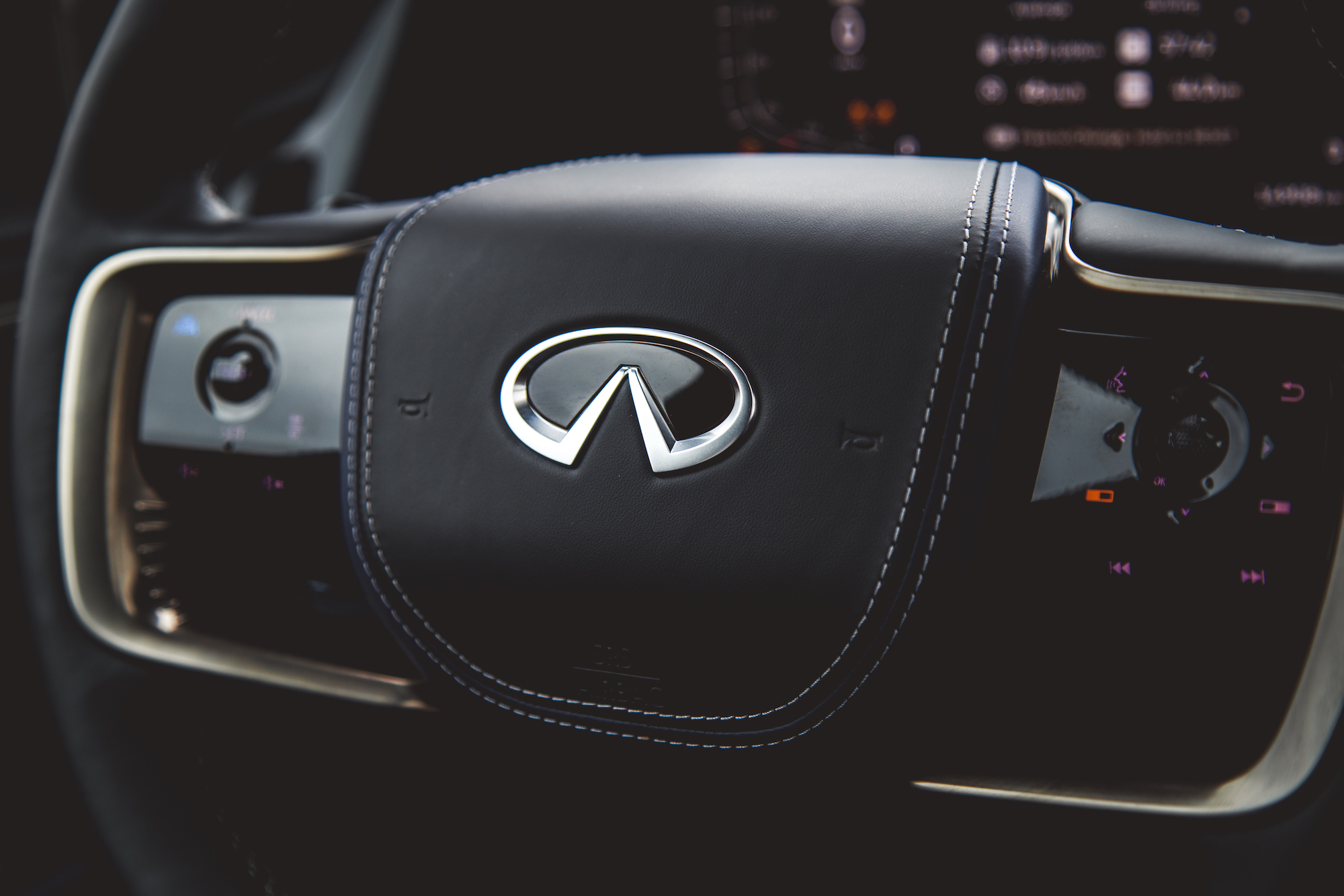 Primer plano del volante de un automóvil Infiniti con el logotipo y los botones de control.