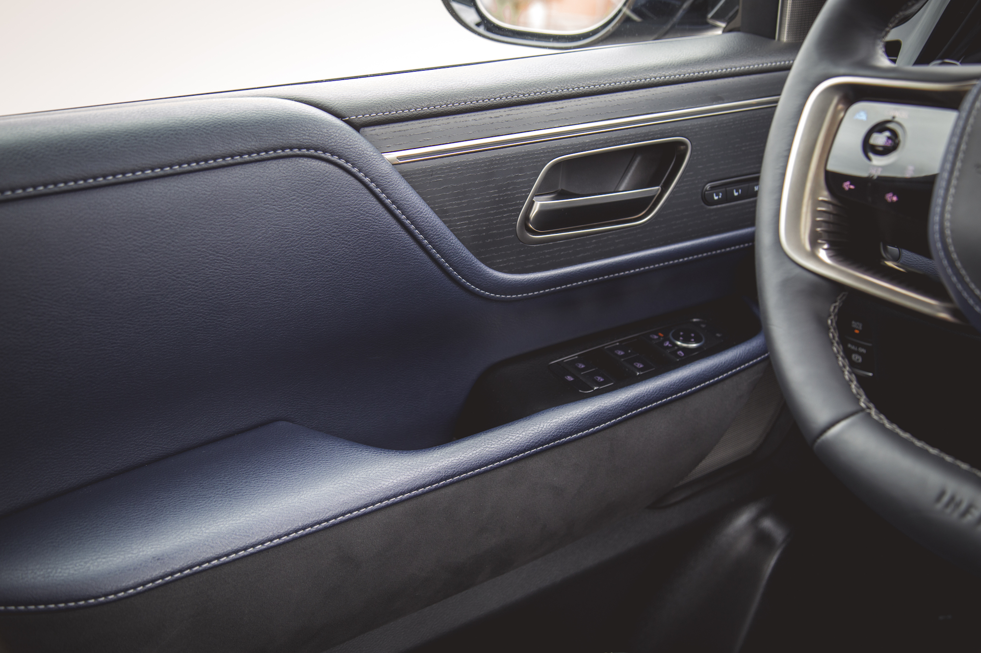 Primer plano del interior de la puerta de un automóvil con cuero texturizado, manija cromada y controles de ventana.