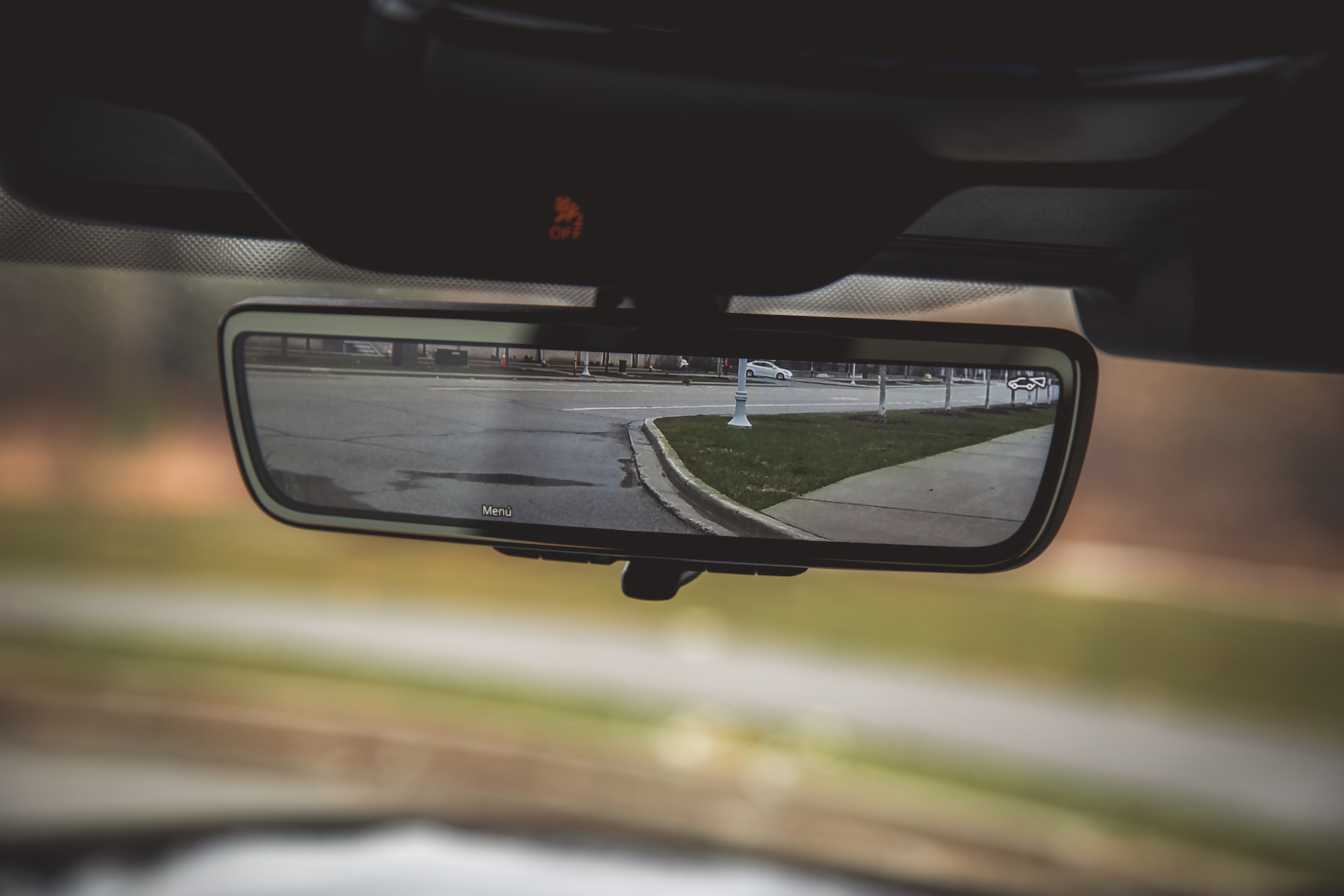 Vista interior del espejo retrovisor de un automóvil que muestra una carretera y una farola al fondo.