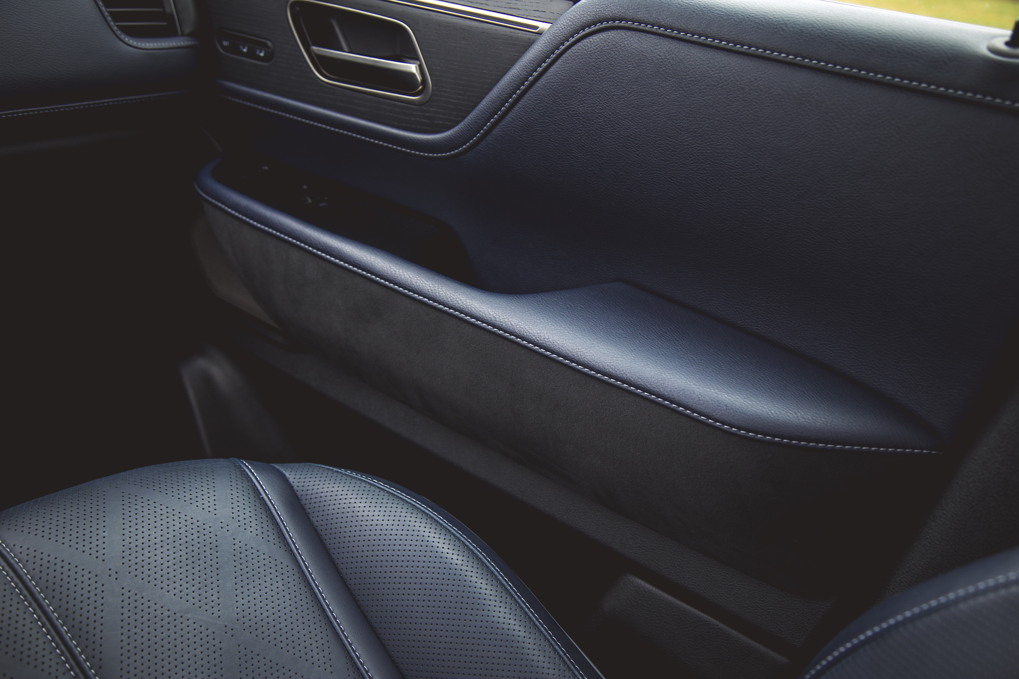 Vista cercana del interior de un automóvil con reposabrazos y asiento de cuero azul, que resalta los patrones texturizados y las costuras.