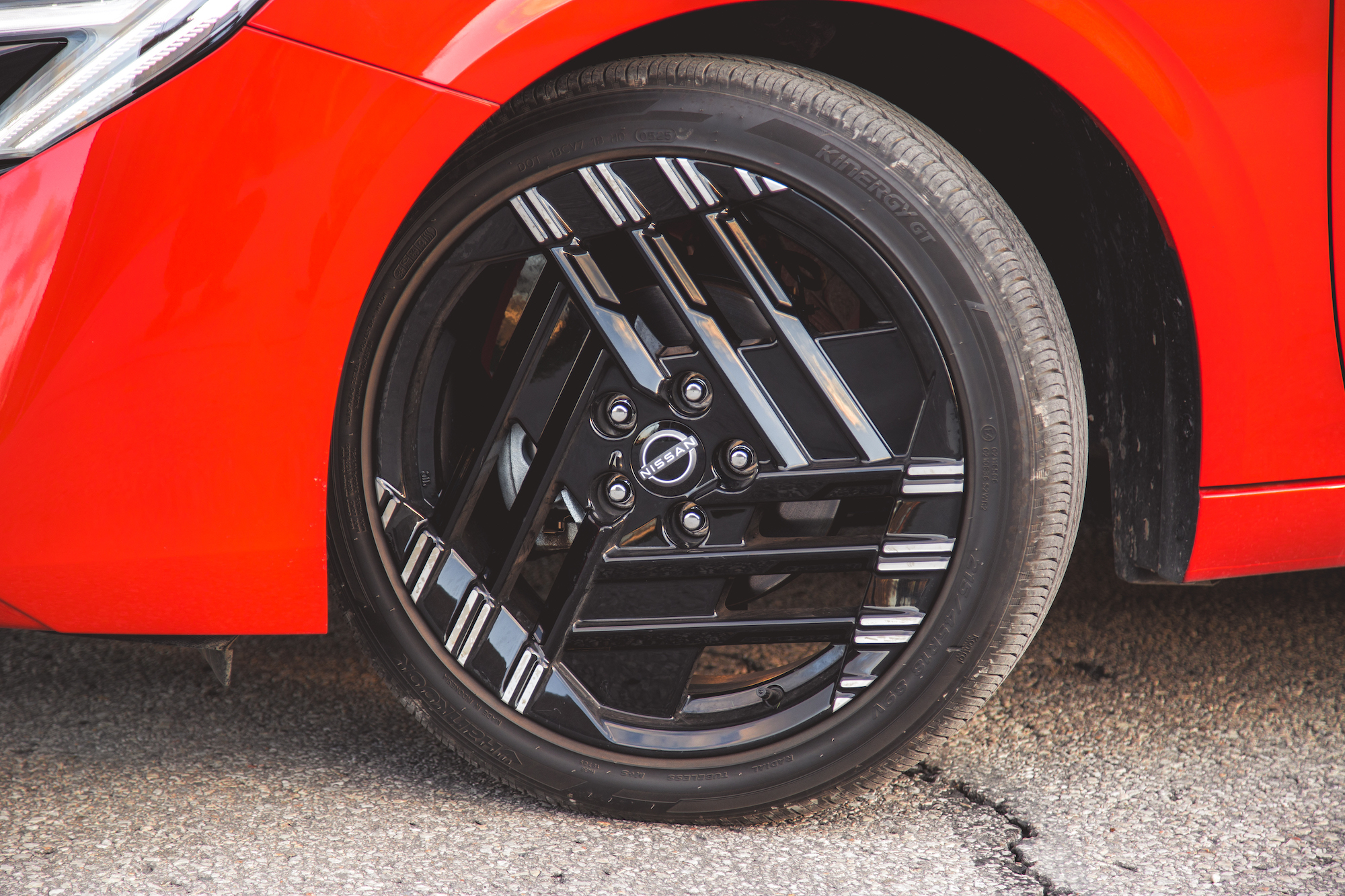 Una vista en primer plano de una llanta de aleación negra con un diseño distintivo en un automóvil rojo, que muestra los detalles del neumático y la rueda.