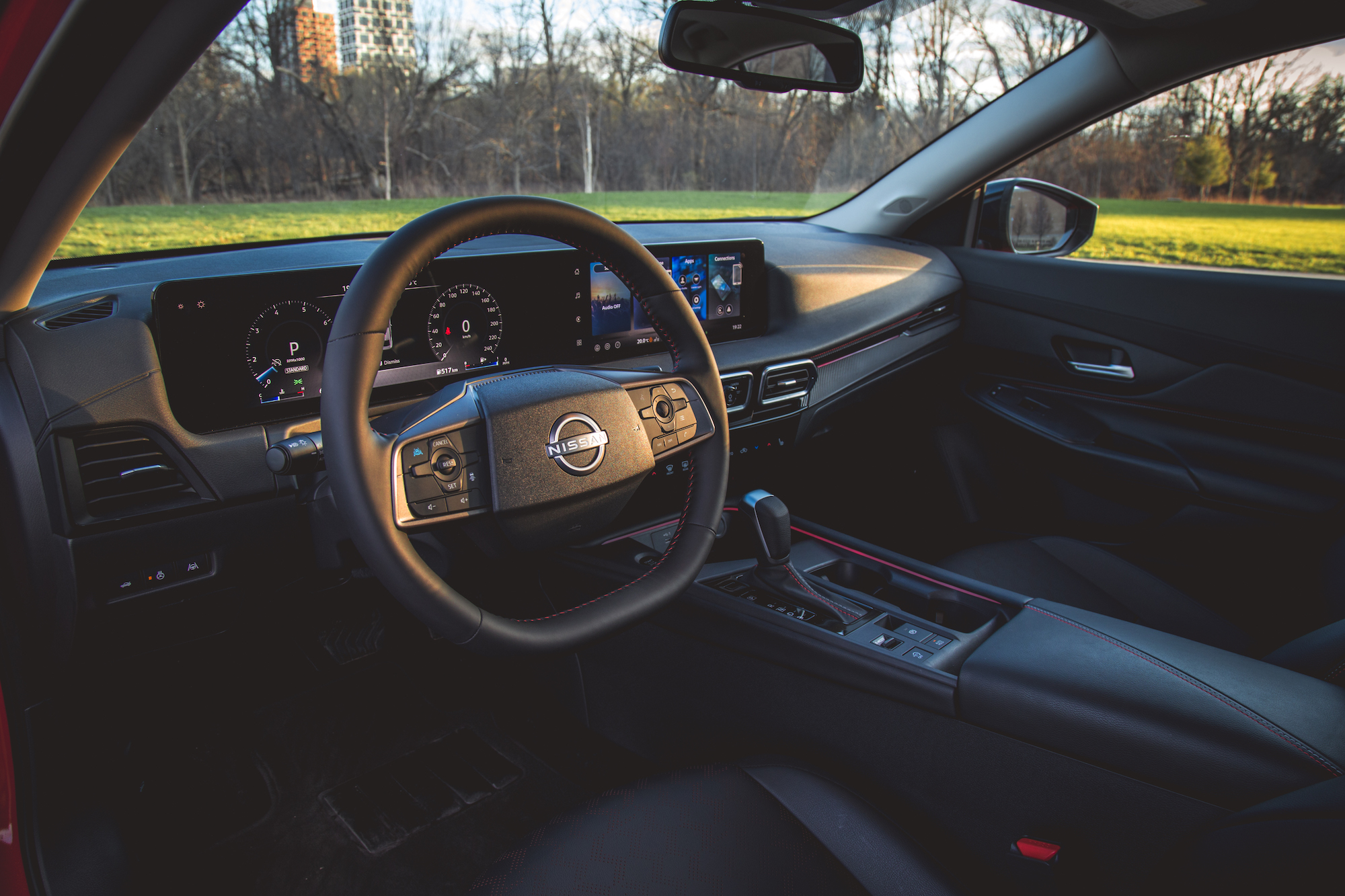 Vista interior de un automóvil Nissan, que muestra el volante, el tablero con pantallas digitales y la palanca de cambios.